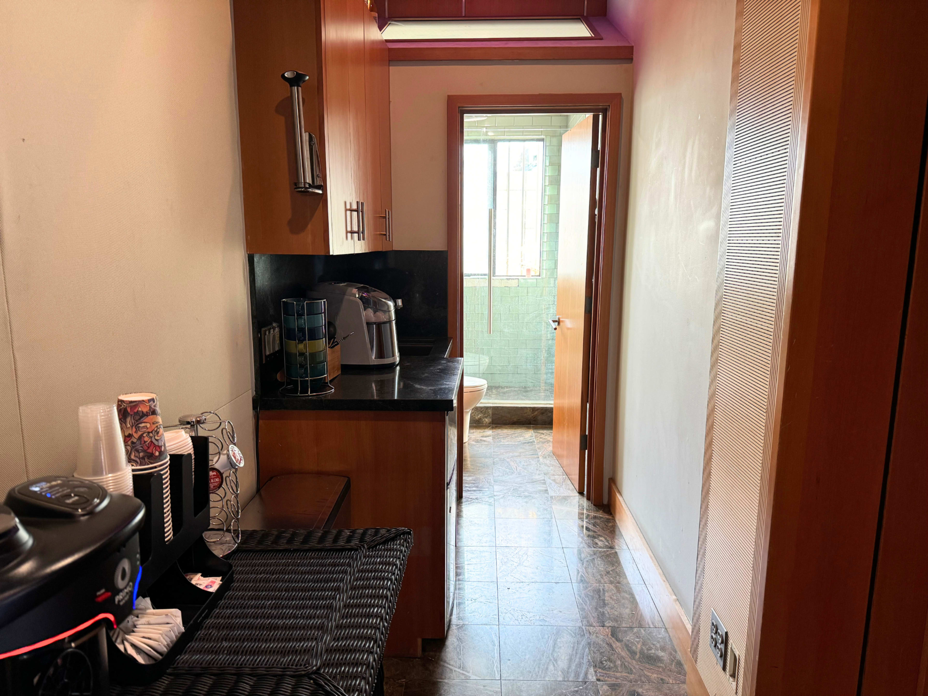 The image shows a narrow kitchen corridor with wooden cabinets on one side and a doorway leading to another room at the end.