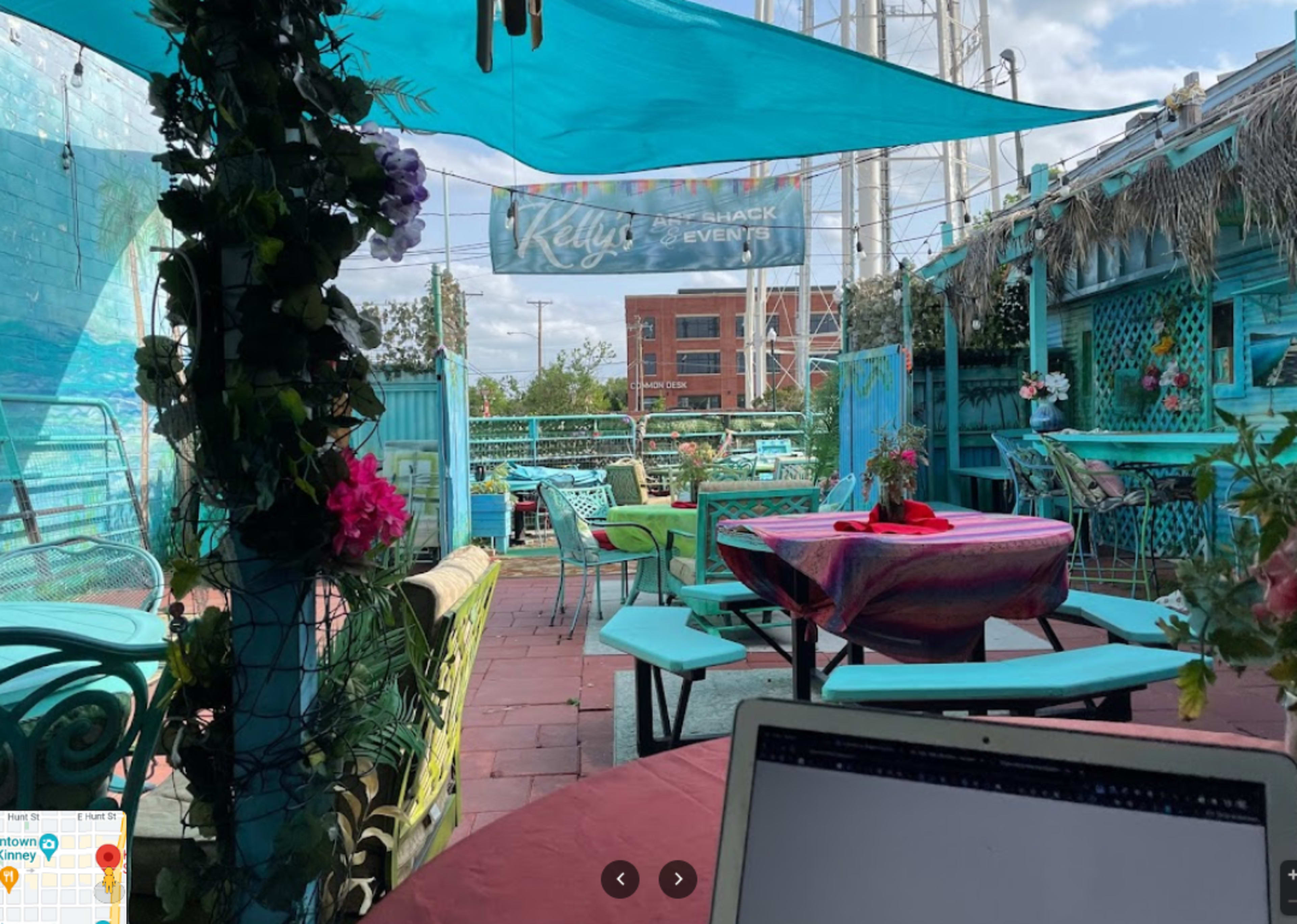 A colorful outdoor patio with turquoise furniture, tables covered with vibrant tablecloths, and decorated with plants and flowers.