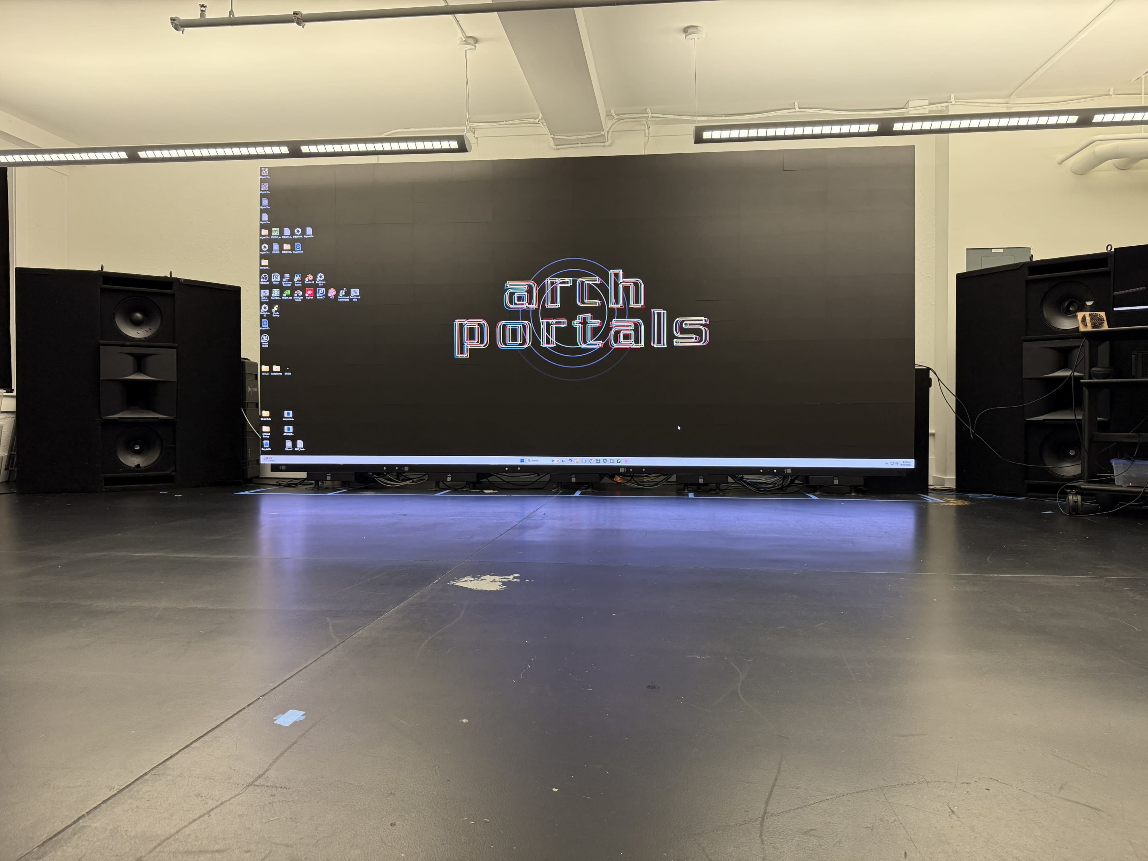 The image shows a large digital screen displaying the text "arch portals," flanked by two large speakers in a studio setting.
