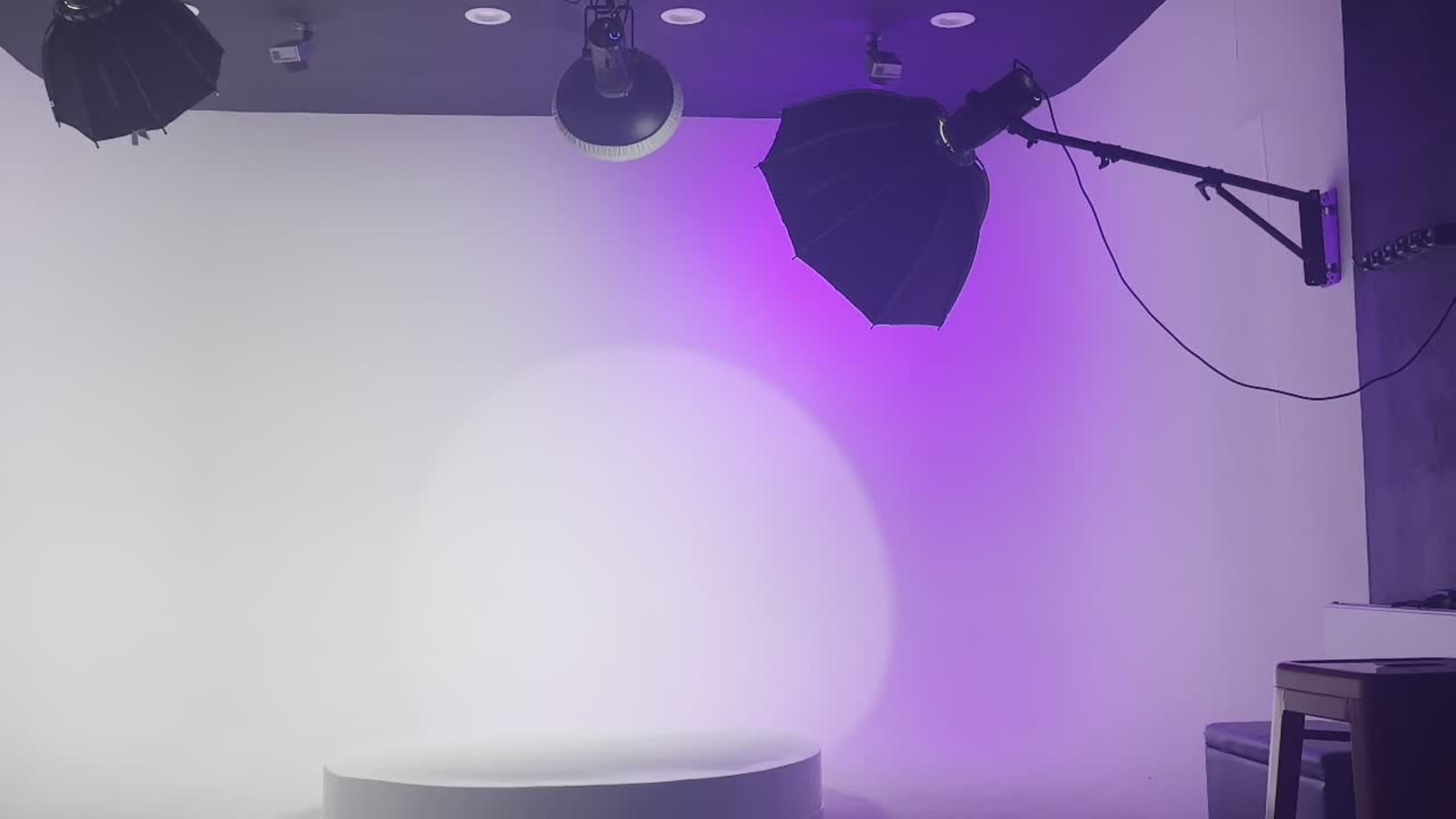 A photography studio is set up with stage lights positioned above and a circular platform in the center against a gradient backdrop.