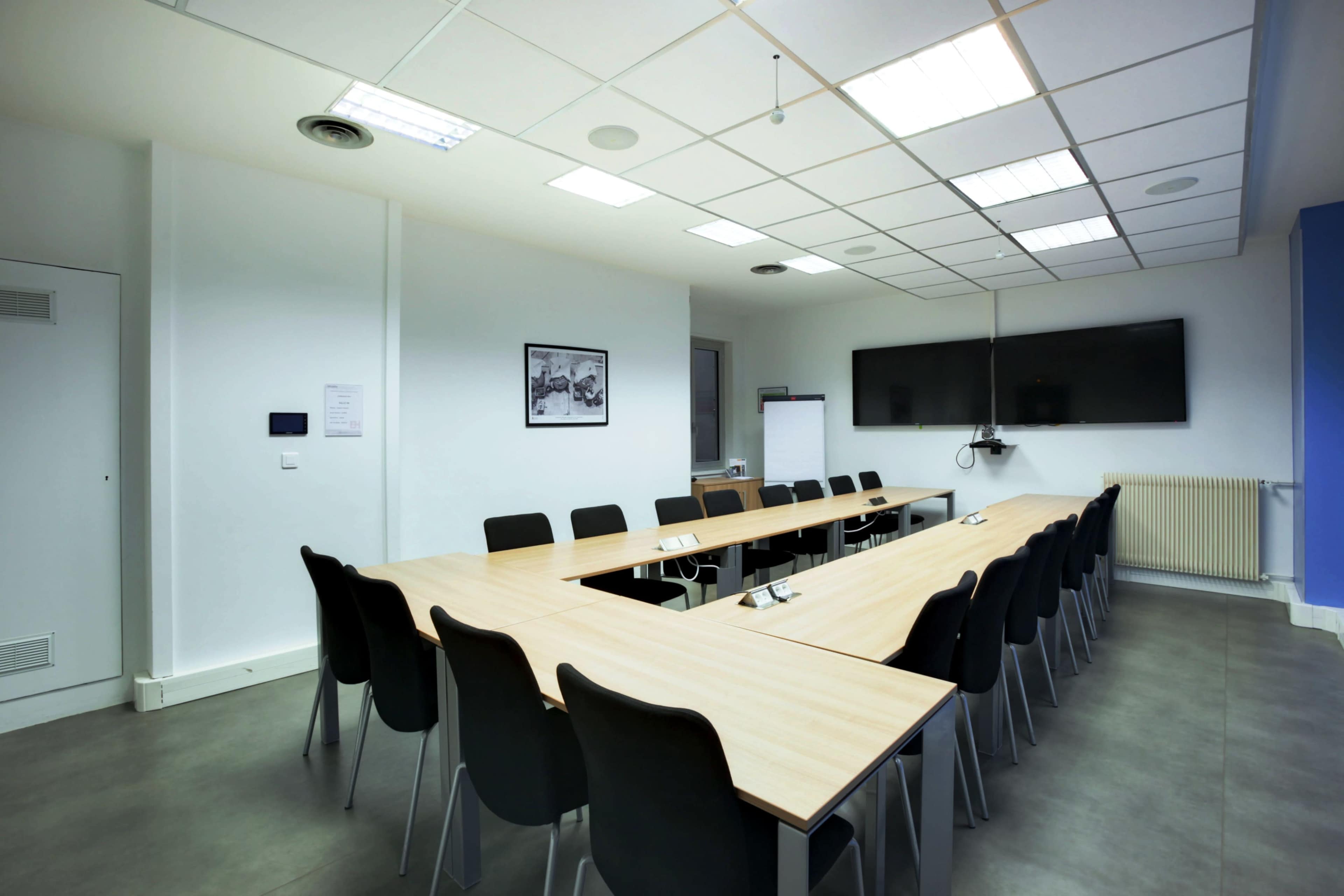 A large conference room features a rectangular table surrounded by black chairs, with a whiteboard and a television mounted on the wall.