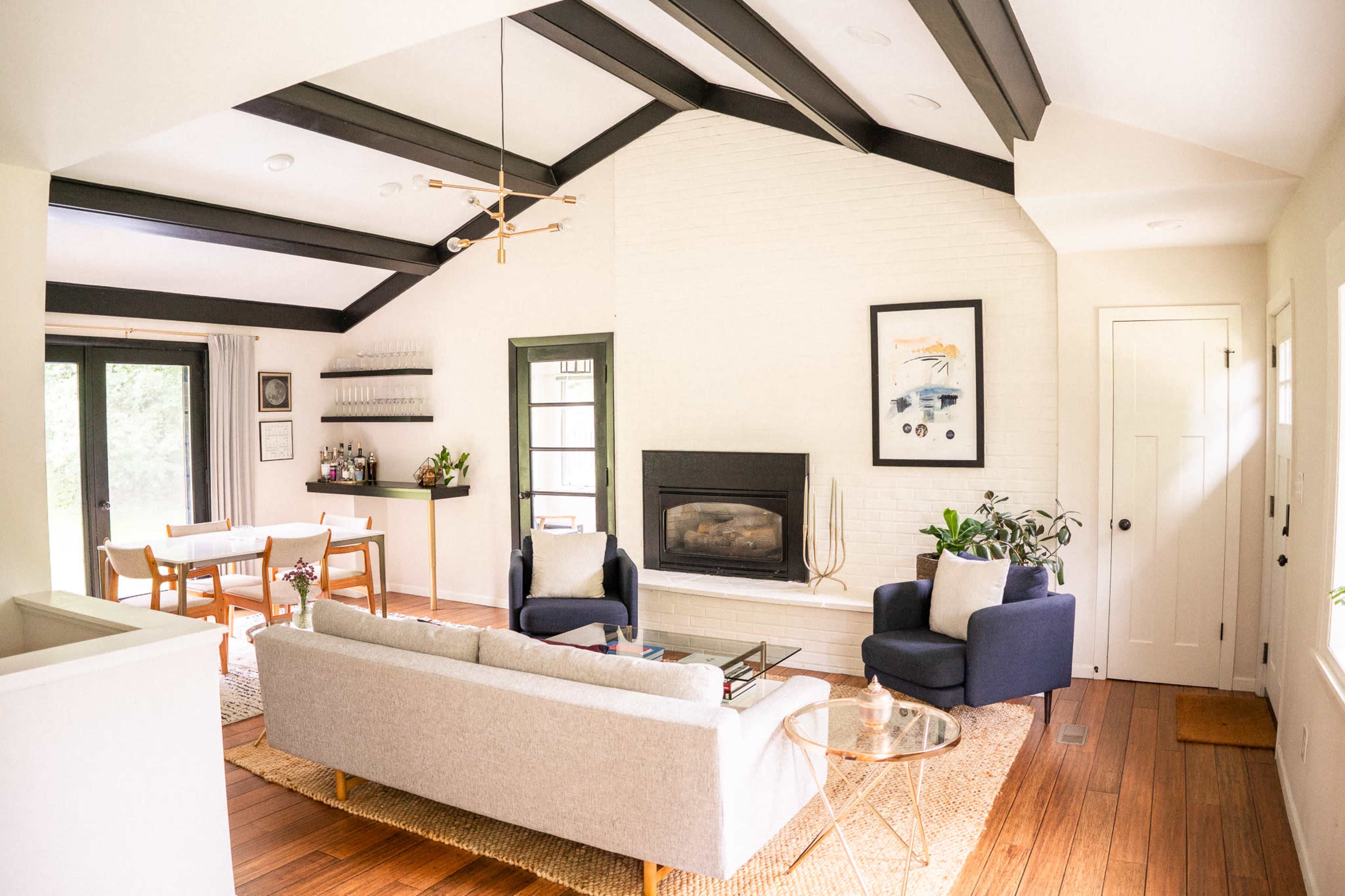 A modern living room features a light-colored sofa, two dark blue chairs, a fireplace, and a dining area with a wooden table in the background.