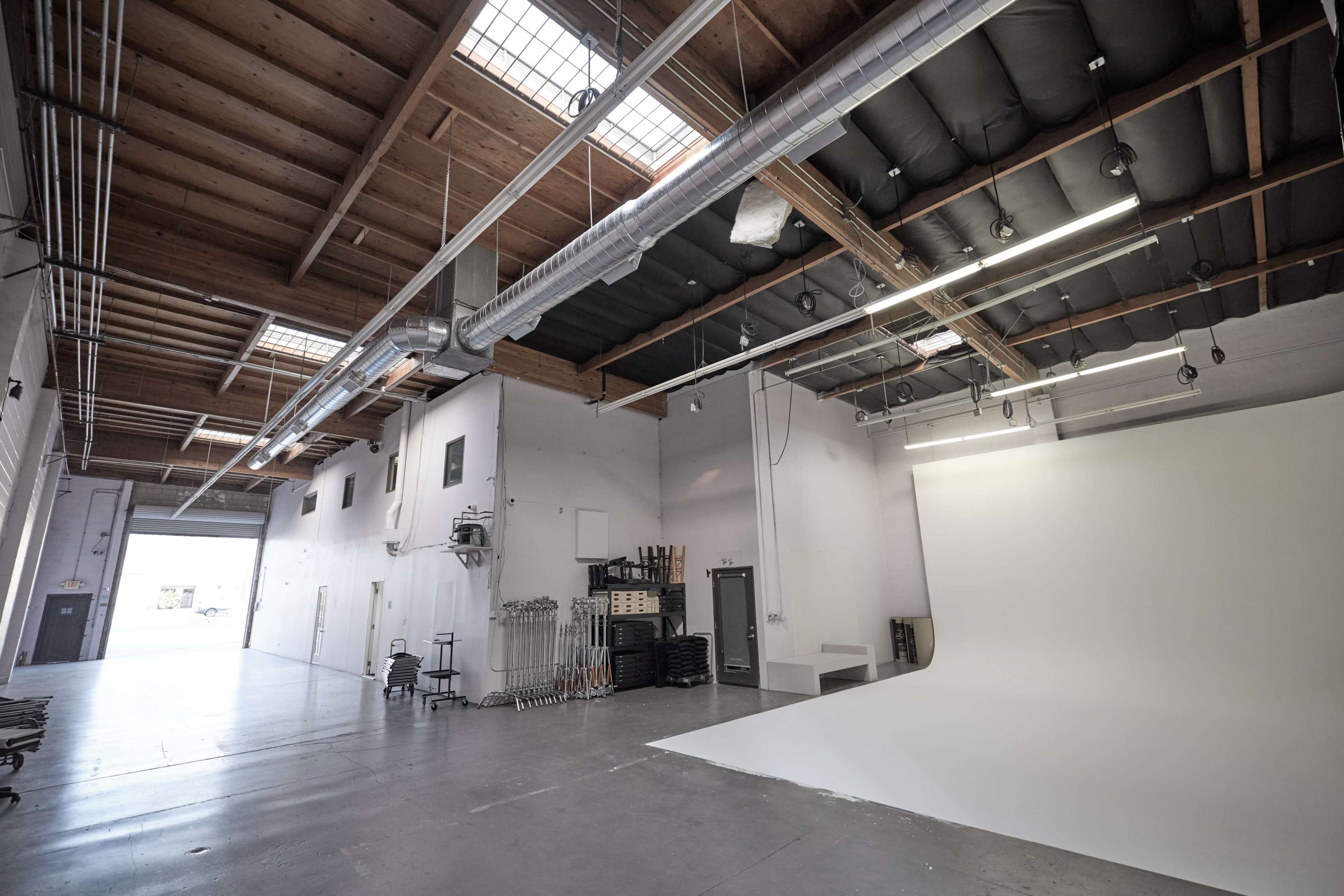 A spacious photography studio with a white backdrop, overhead lighting, and exposed wooden beams.