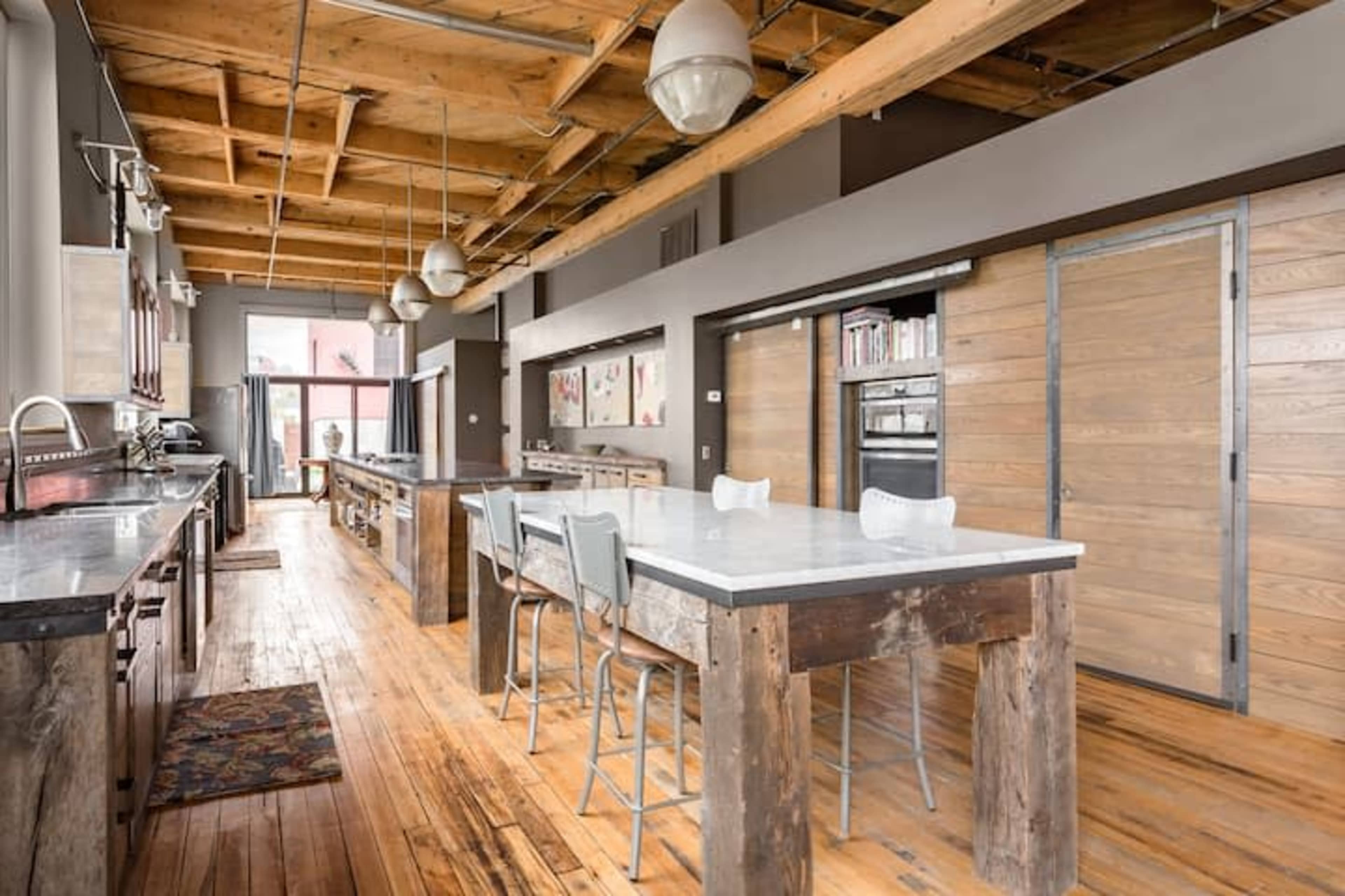 A spacious kitchen featuring wood beams, concrete countertops, and a long island with bar stools.