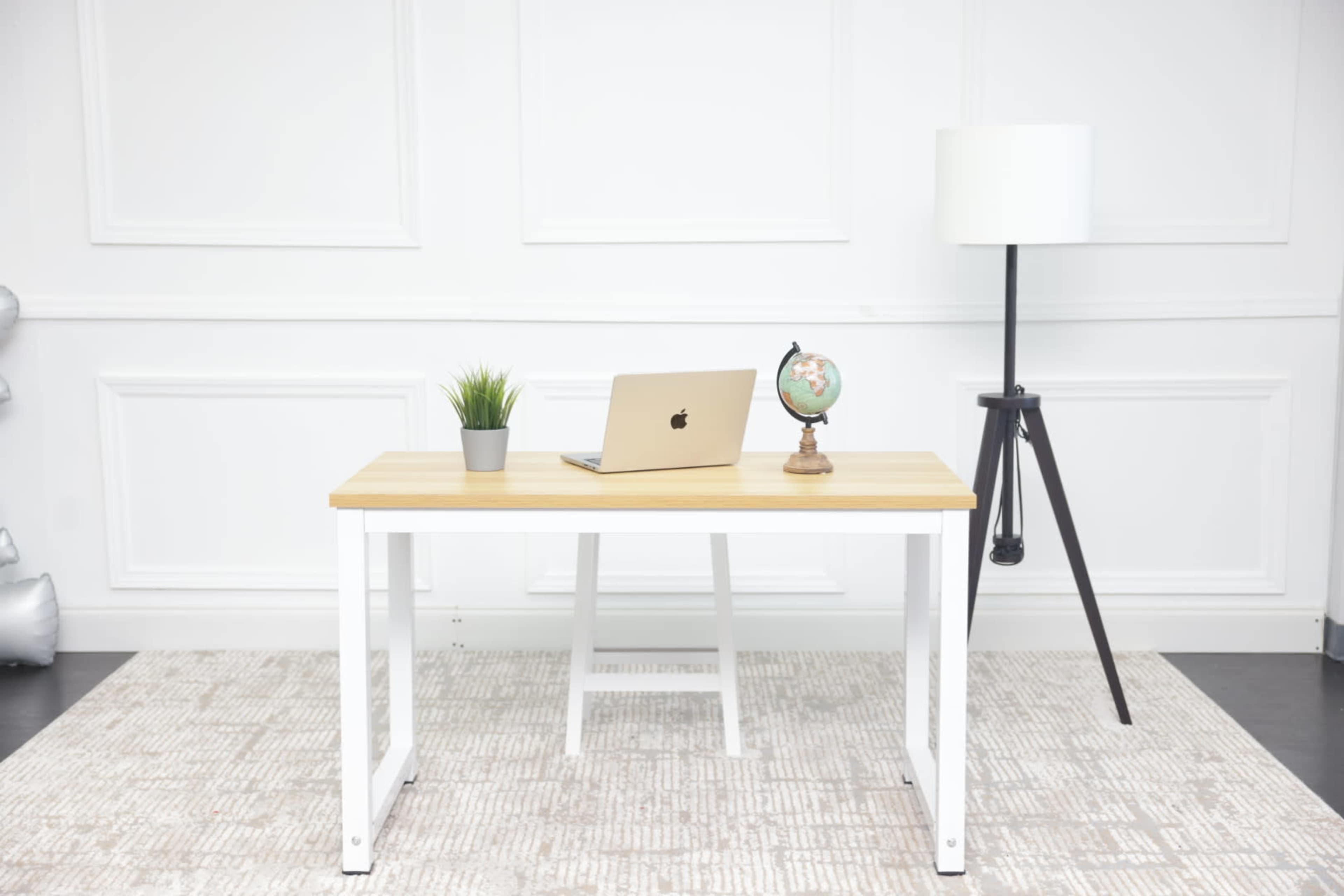 A modern desk with a laptop, a small globe, a potted plant, and a lamp is positioned in a bright, minimalist room.