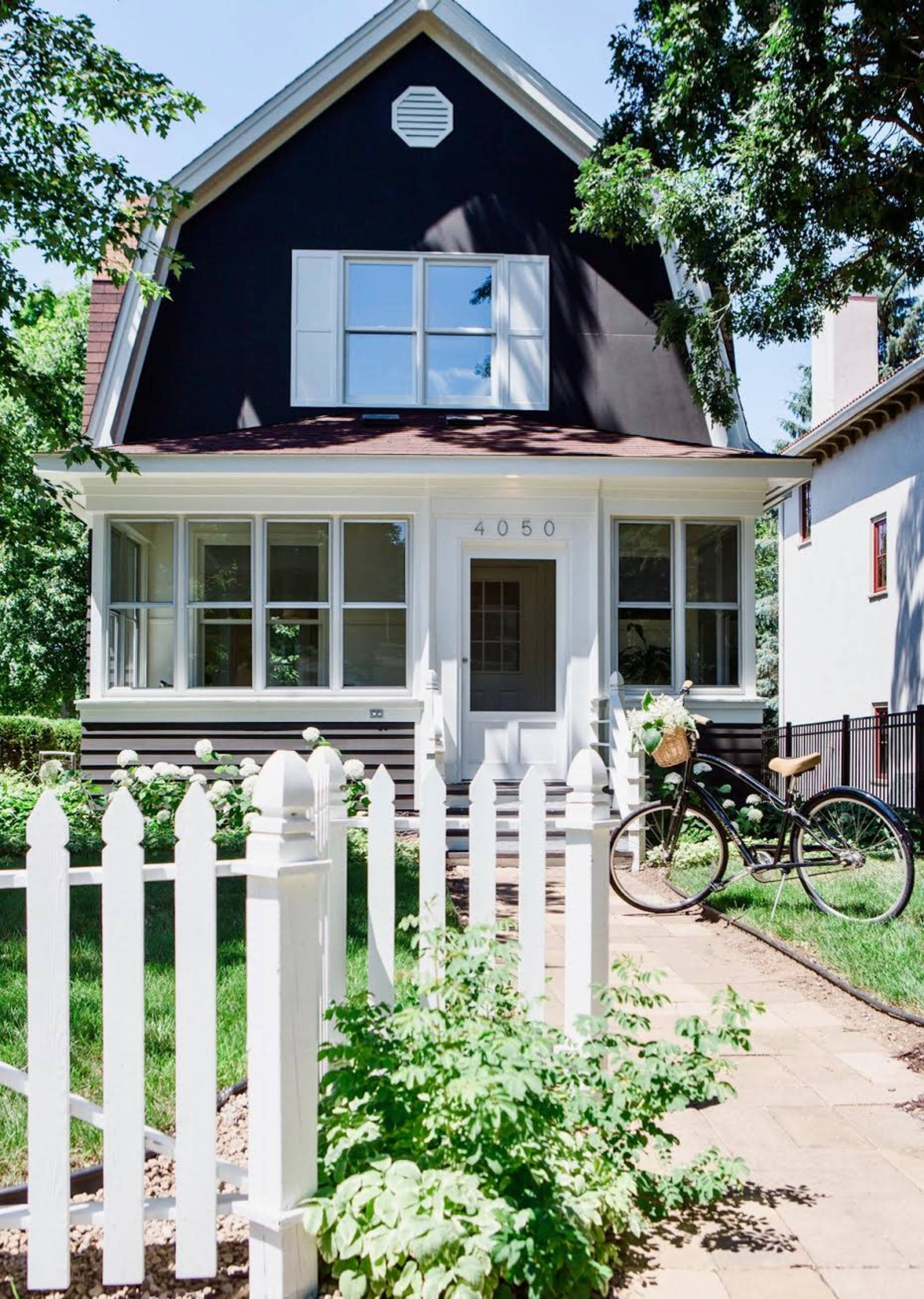 A black-painted house with white trim features a picket fence and a bicycle parked alongside a stone pathway.