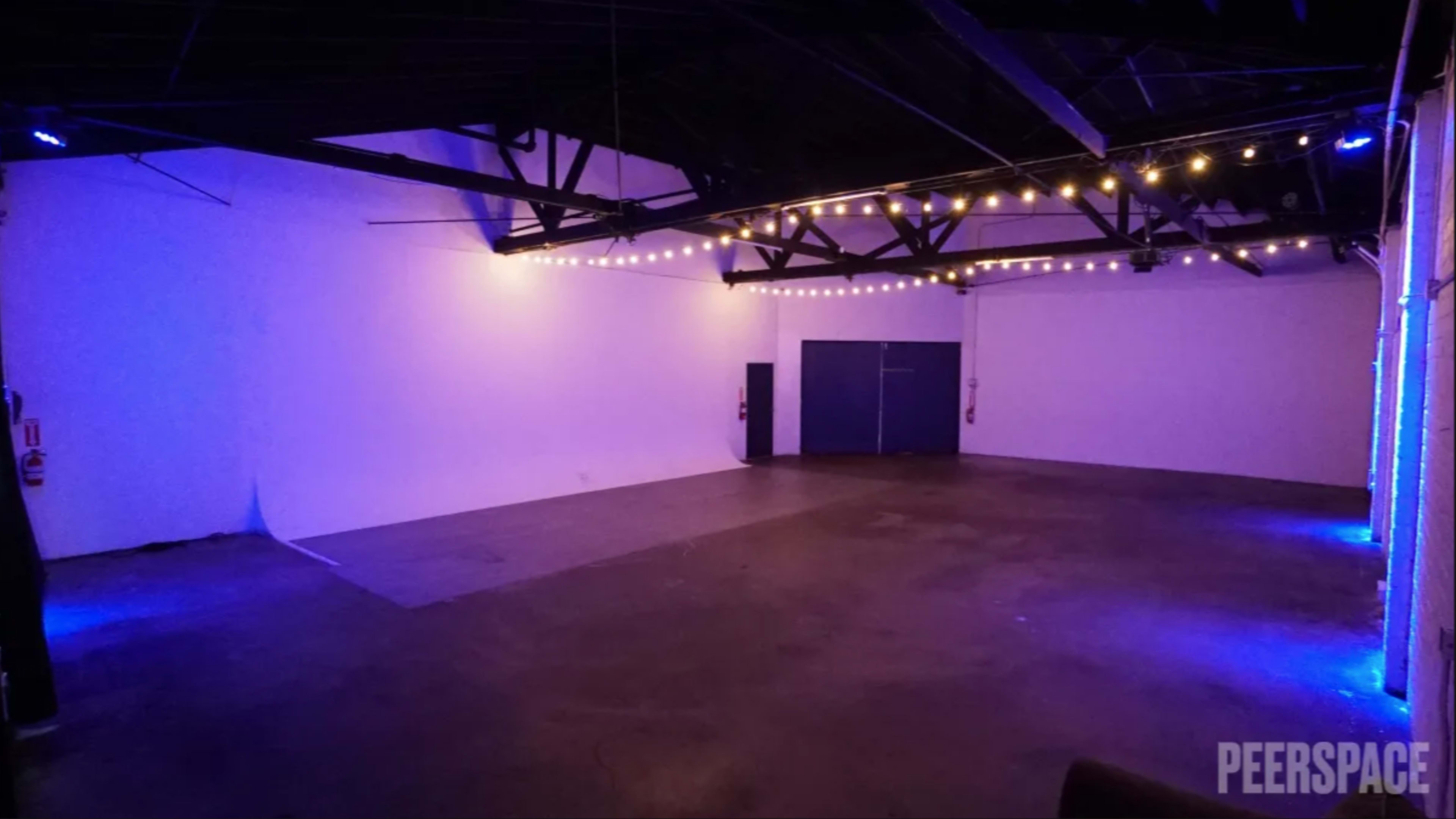 A spacious, empty venue with a polished concrete floor and purple accent lighting.
