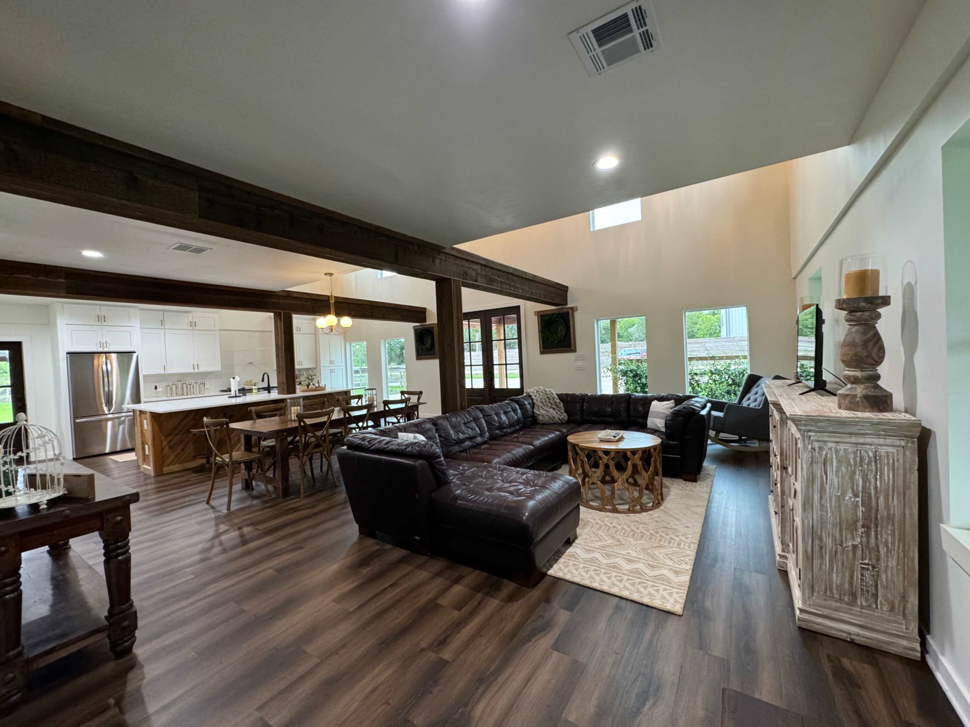 A spacious living area with a dark leather sectional sofa, a wooden dining table, and large windows that provide natural light.