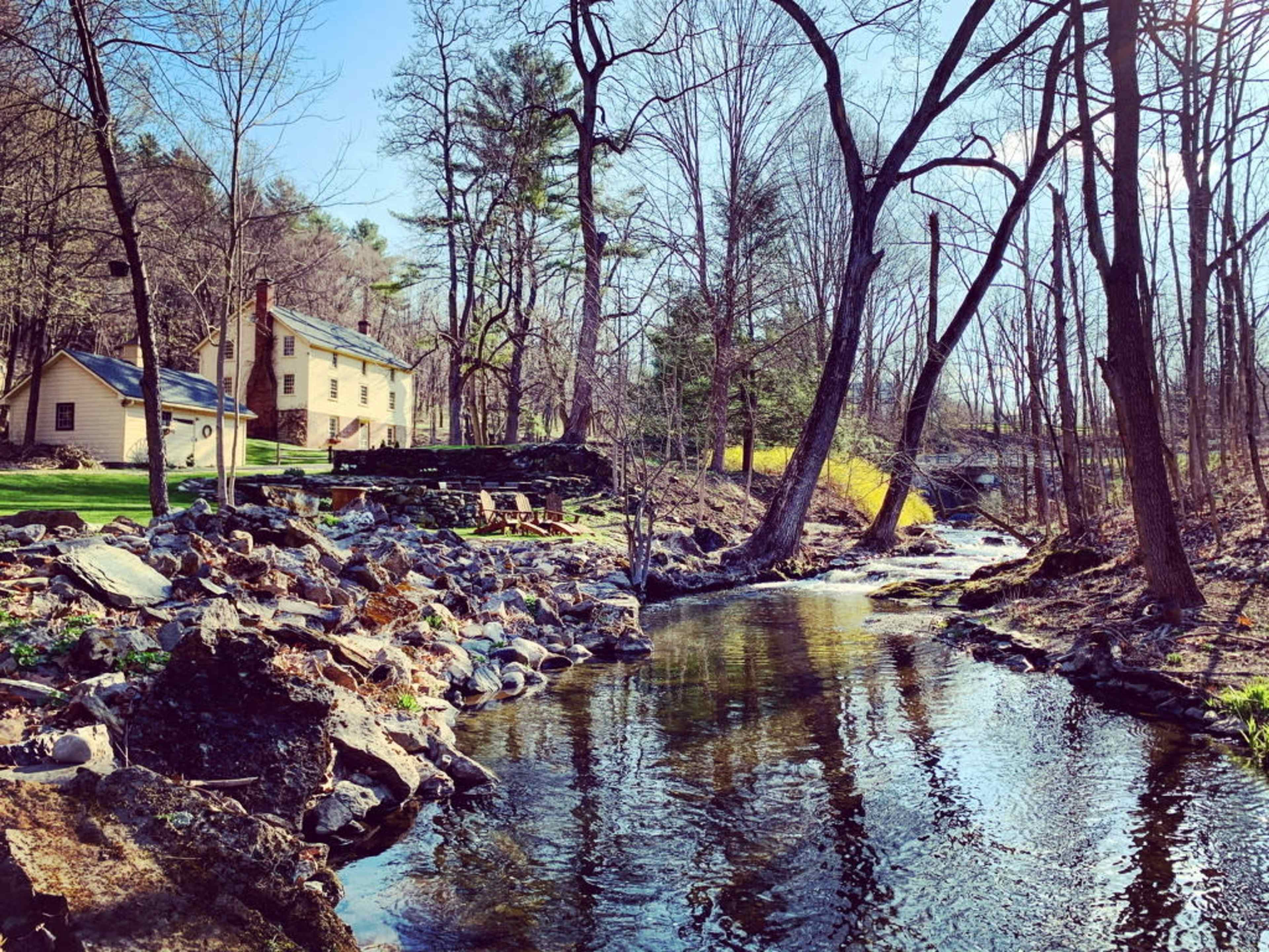 A tranquil stream flows alongside a house, surrounded by trees and rocky terrain.