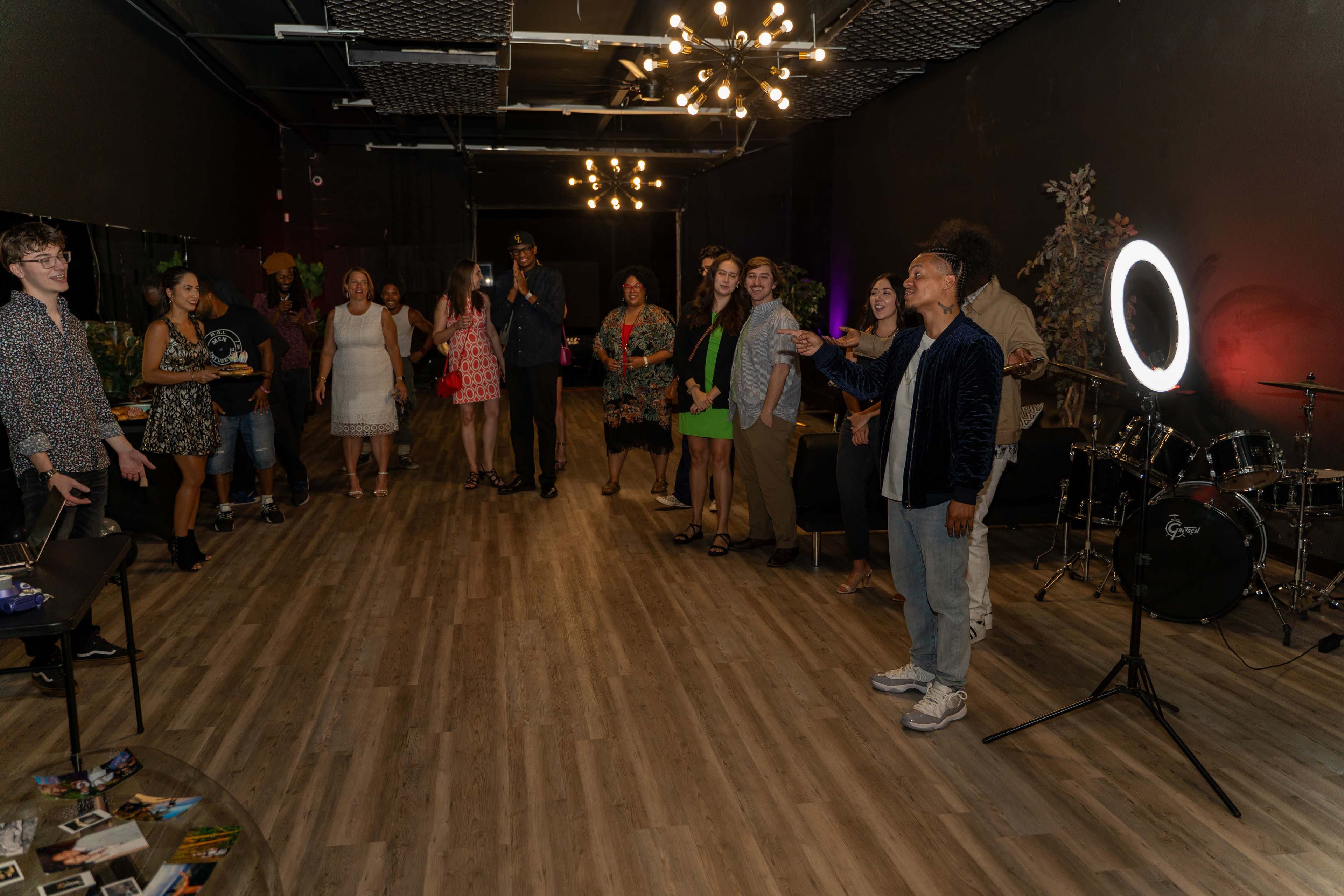 A group of people stands together in a dimly lit room decorated with lights and musical instruments, engaging in conversation and laughter.