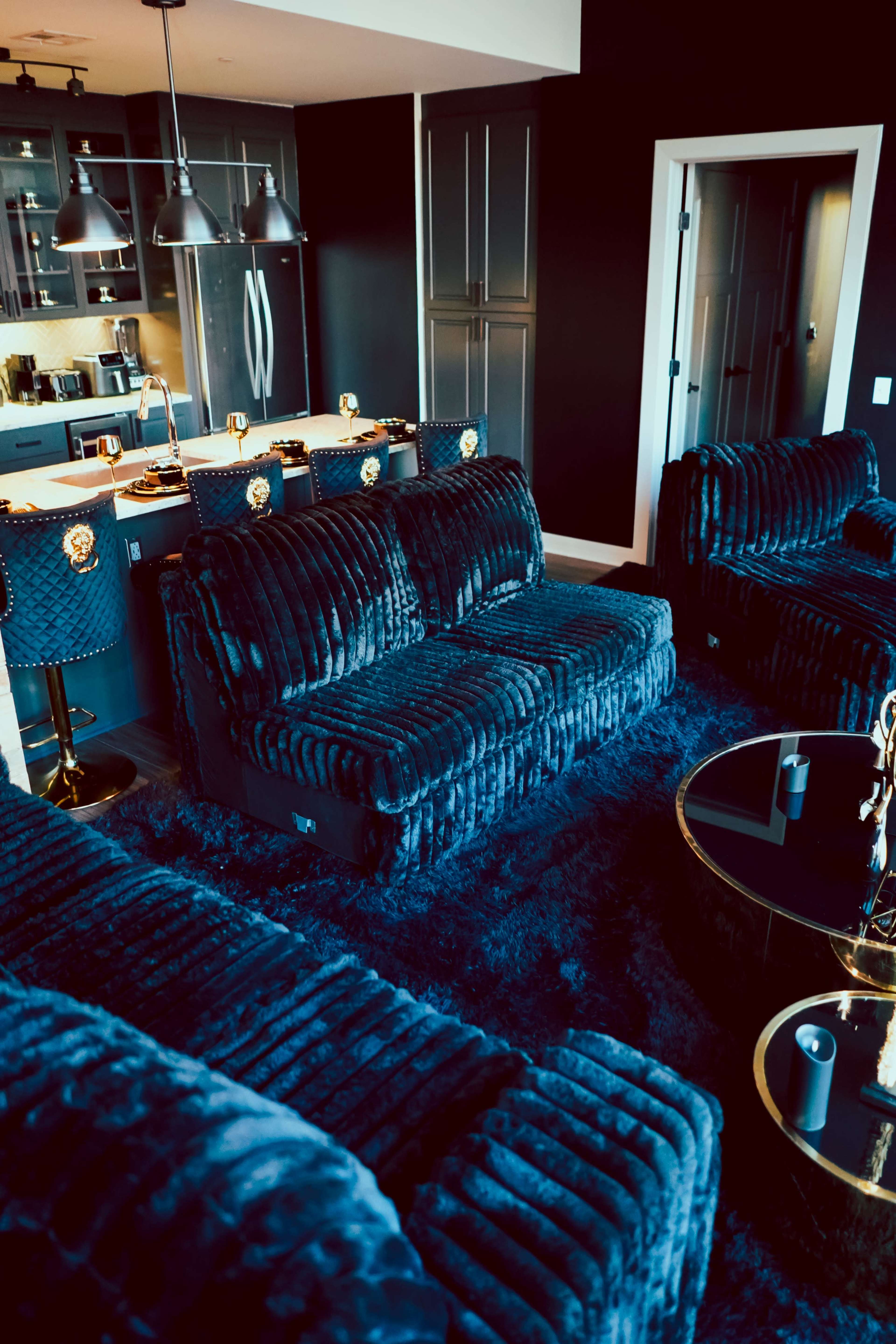 The image features a modern living room with plush, dark blue sofas and a matching area rug, illuminated by pendant lights above a kitchen counter in the background.