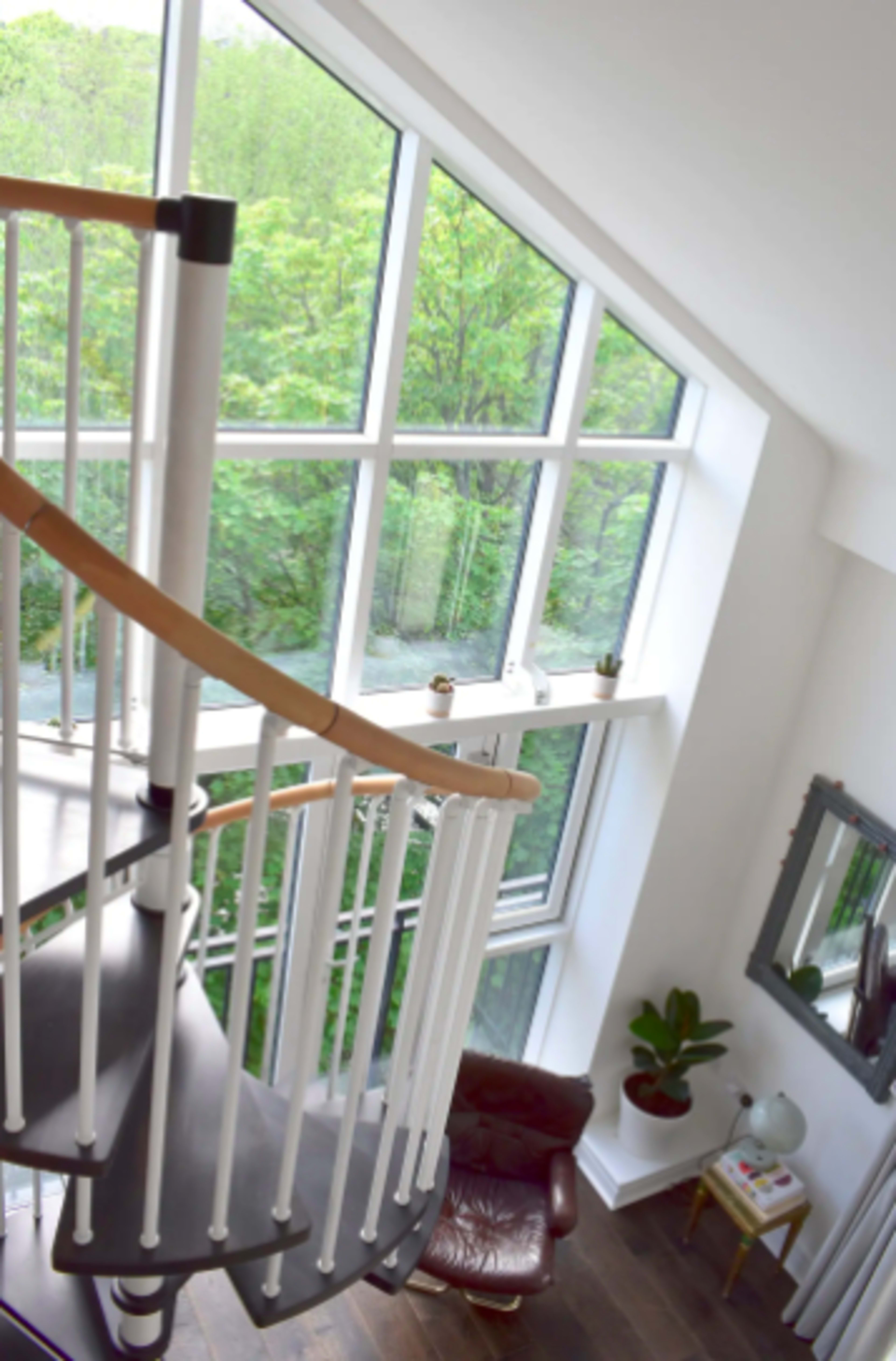 A spiral staircase winds upward beside large windows overlooking a green landscape.