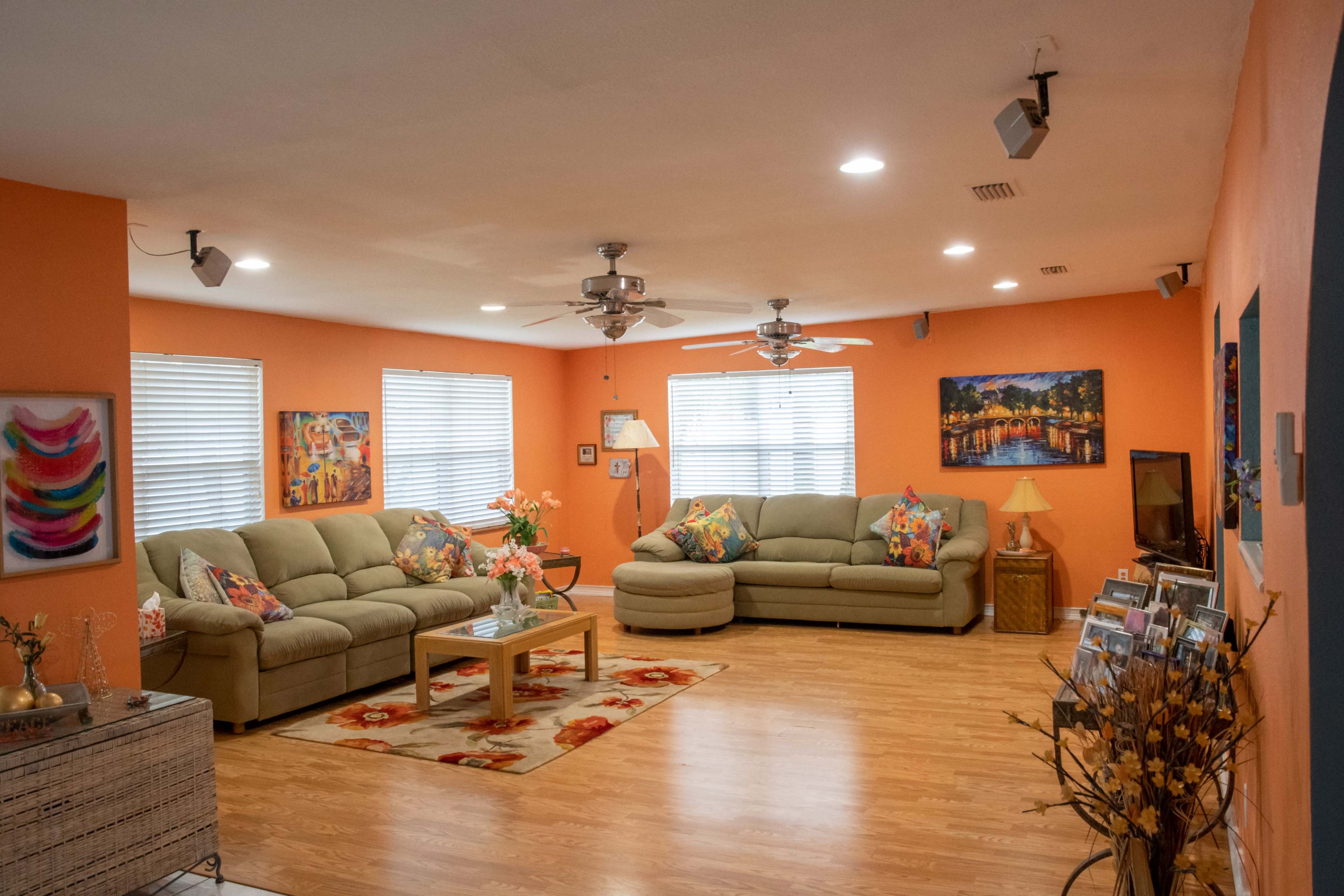 A spacious living room with orange walls, two large sofas adorned with colorful cushions, a coffee table, and framed artwork on the walls.