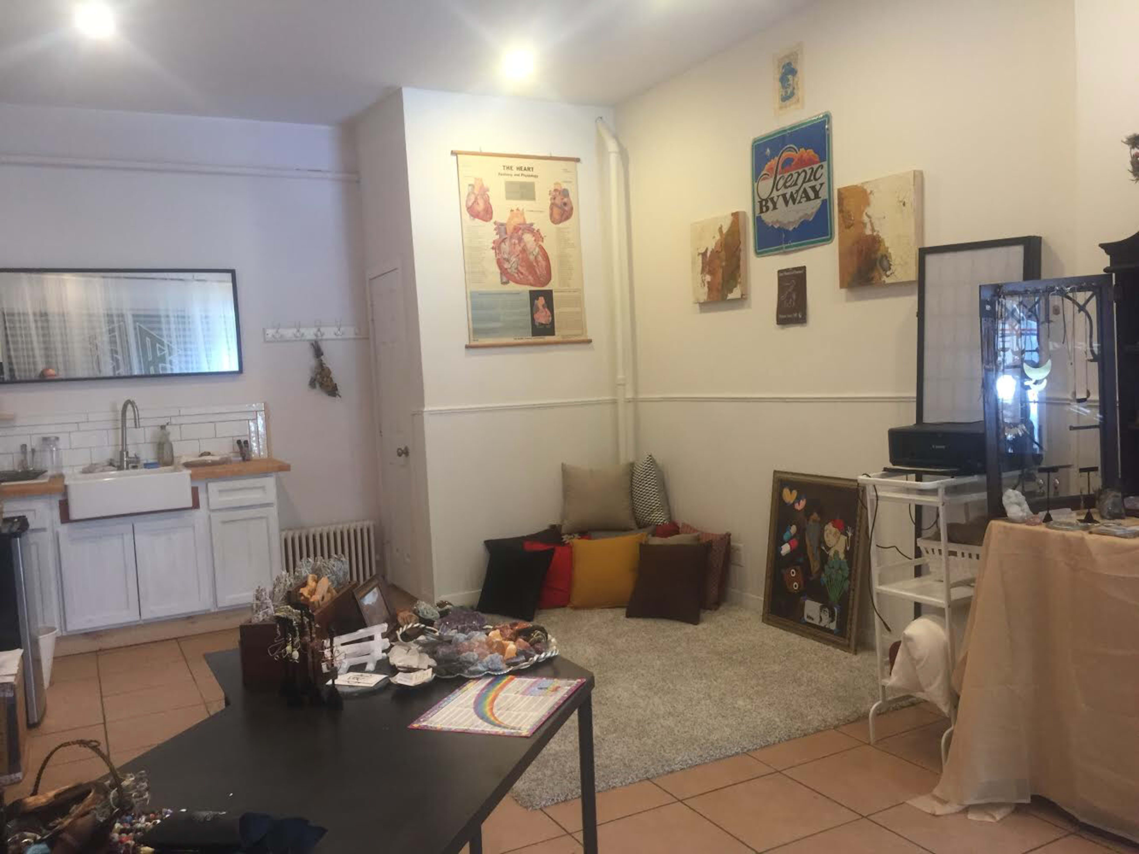 A cozy room with a kitchen area, a seating arrangement with cushions, and various decorative items displayed on tables.