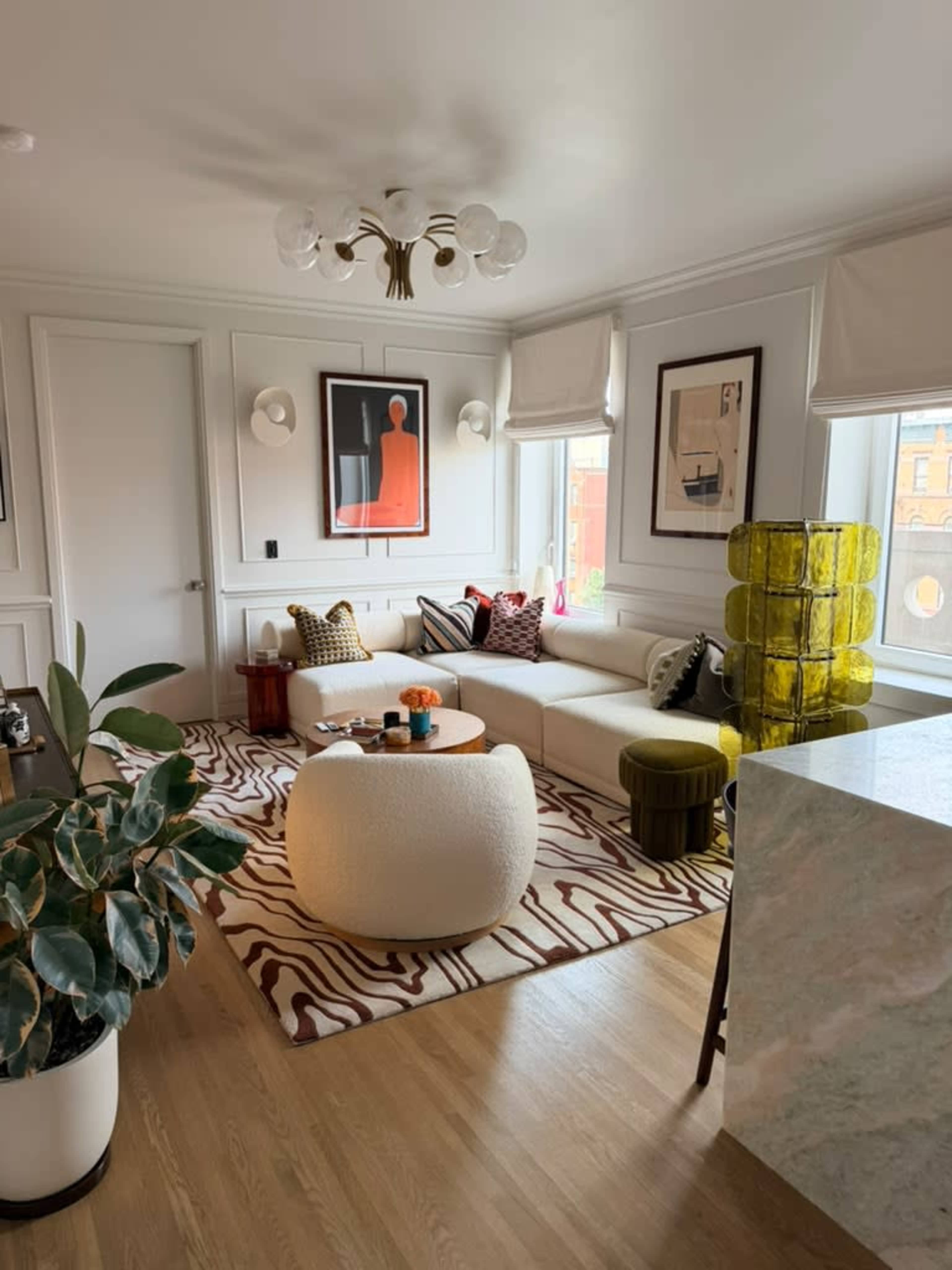 The living room features a sectional sofa, patterned area rug, vibrant decor items, and large windows providing natural light.