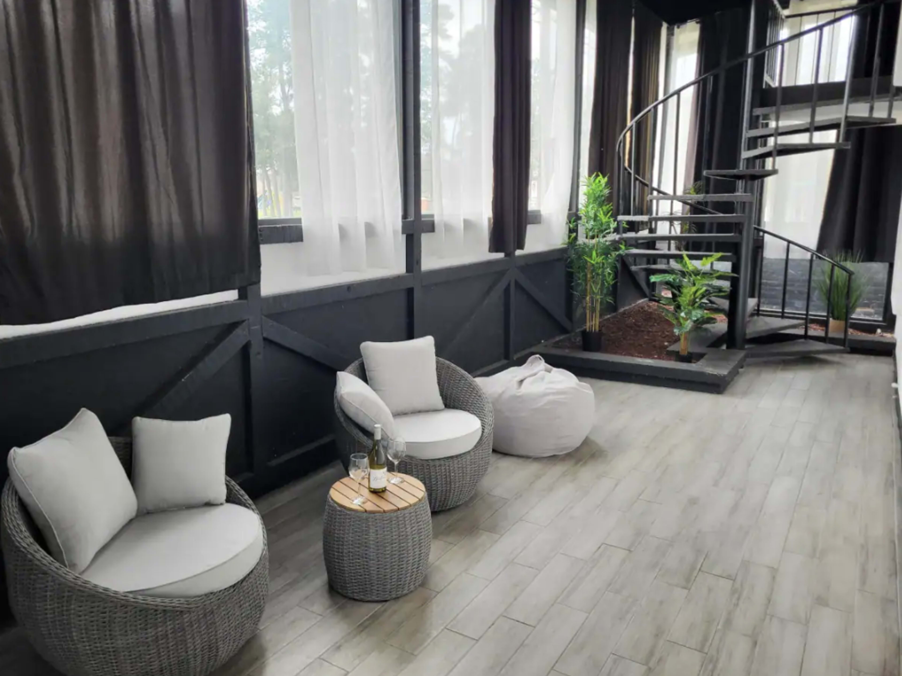 A modern indoor seating area with two round chairs, a small table, a spiral staircase, and a potted plant.