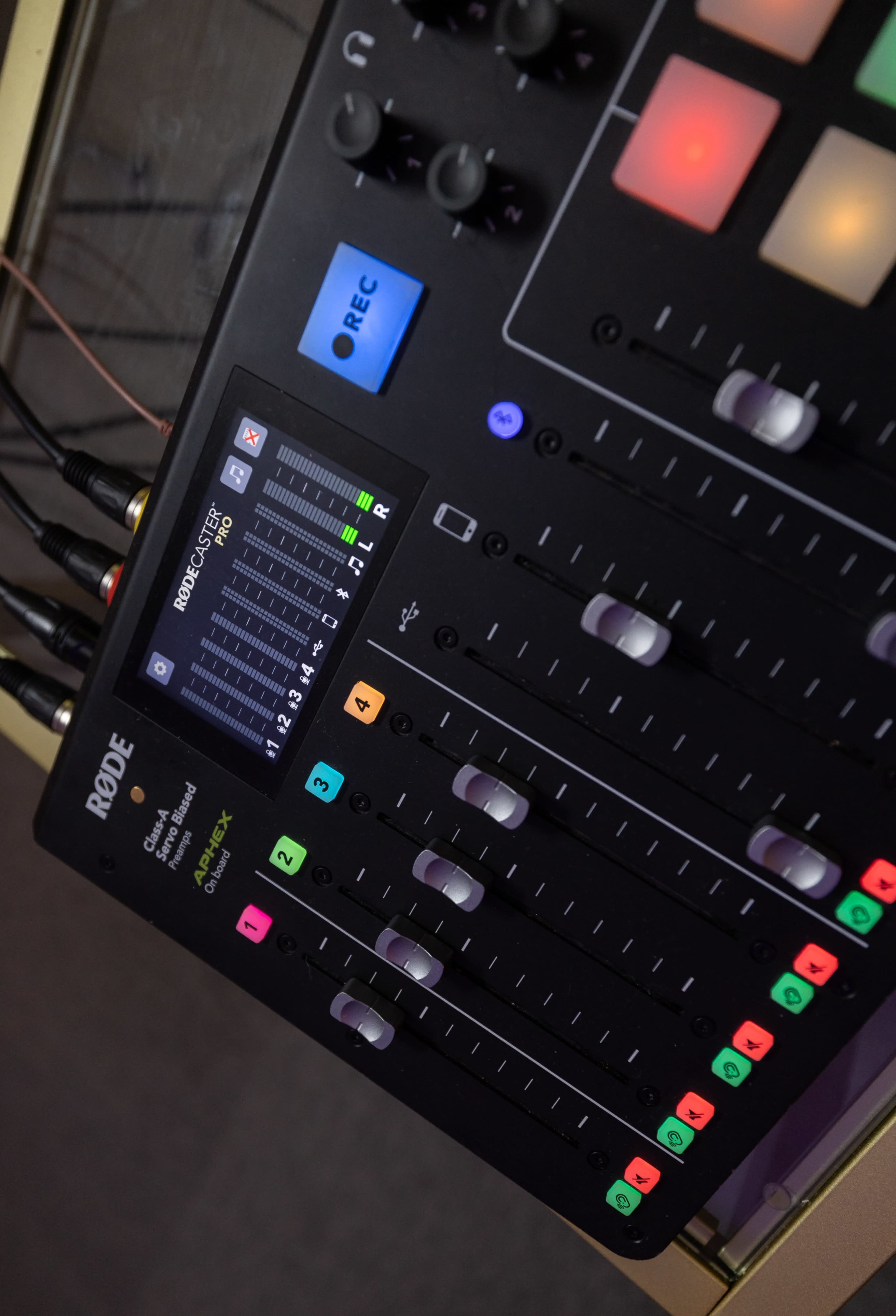 A close-up of a RodeCaster Pro audio mixer with faders, buttons, and a digital display.
