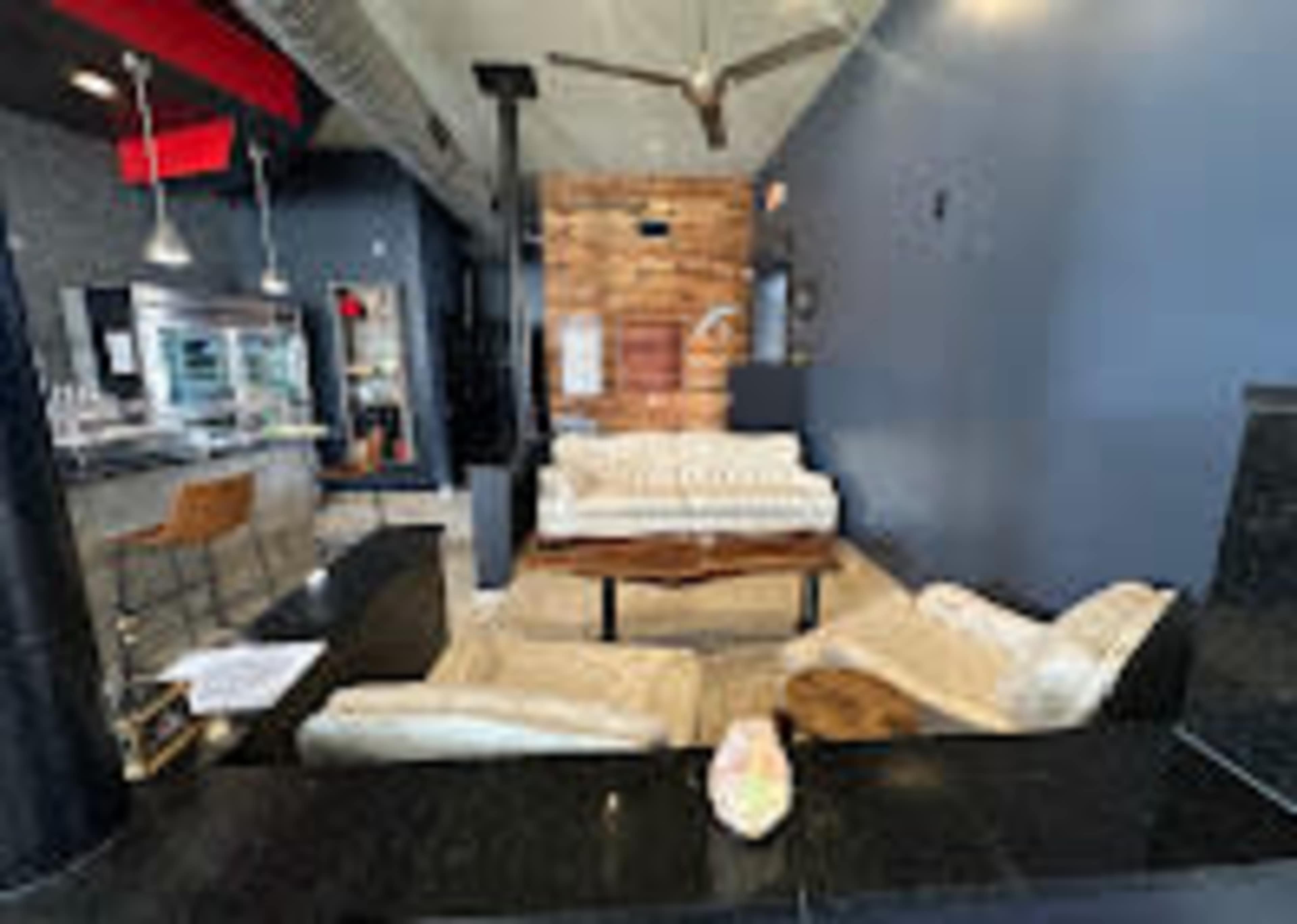The image shows a modern lounge area with a wooden coffee table, plush seating, and a bar in the background.