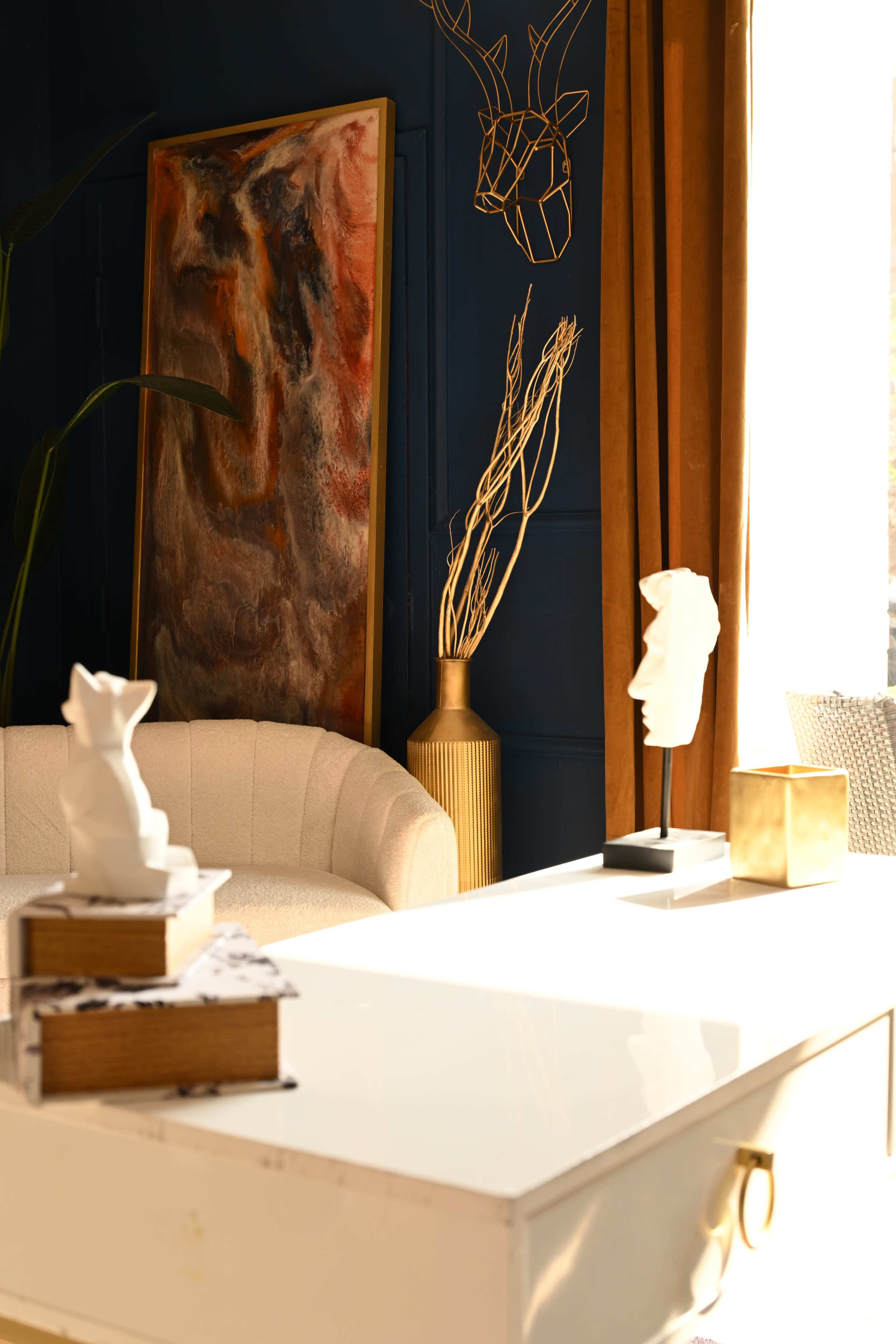 The image shows a modern office space featuring a white desk, a beige curved chair, an abstract painting, and decorative items such as a sculpture and a gold vase.