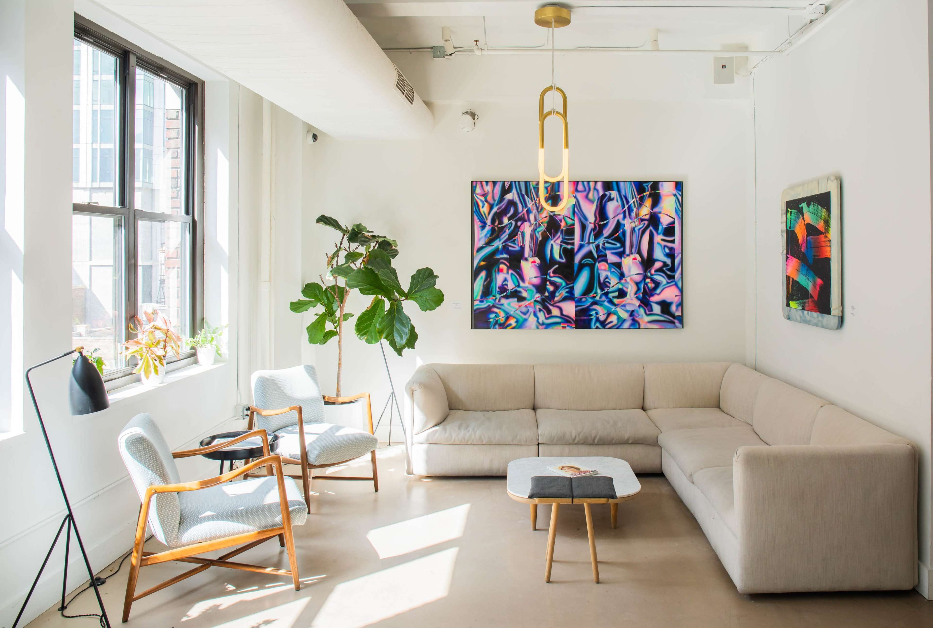 A bright and airy living room features a large sectional sofa, two chairs, a coffee table, and vibrant abstract art on the walls.