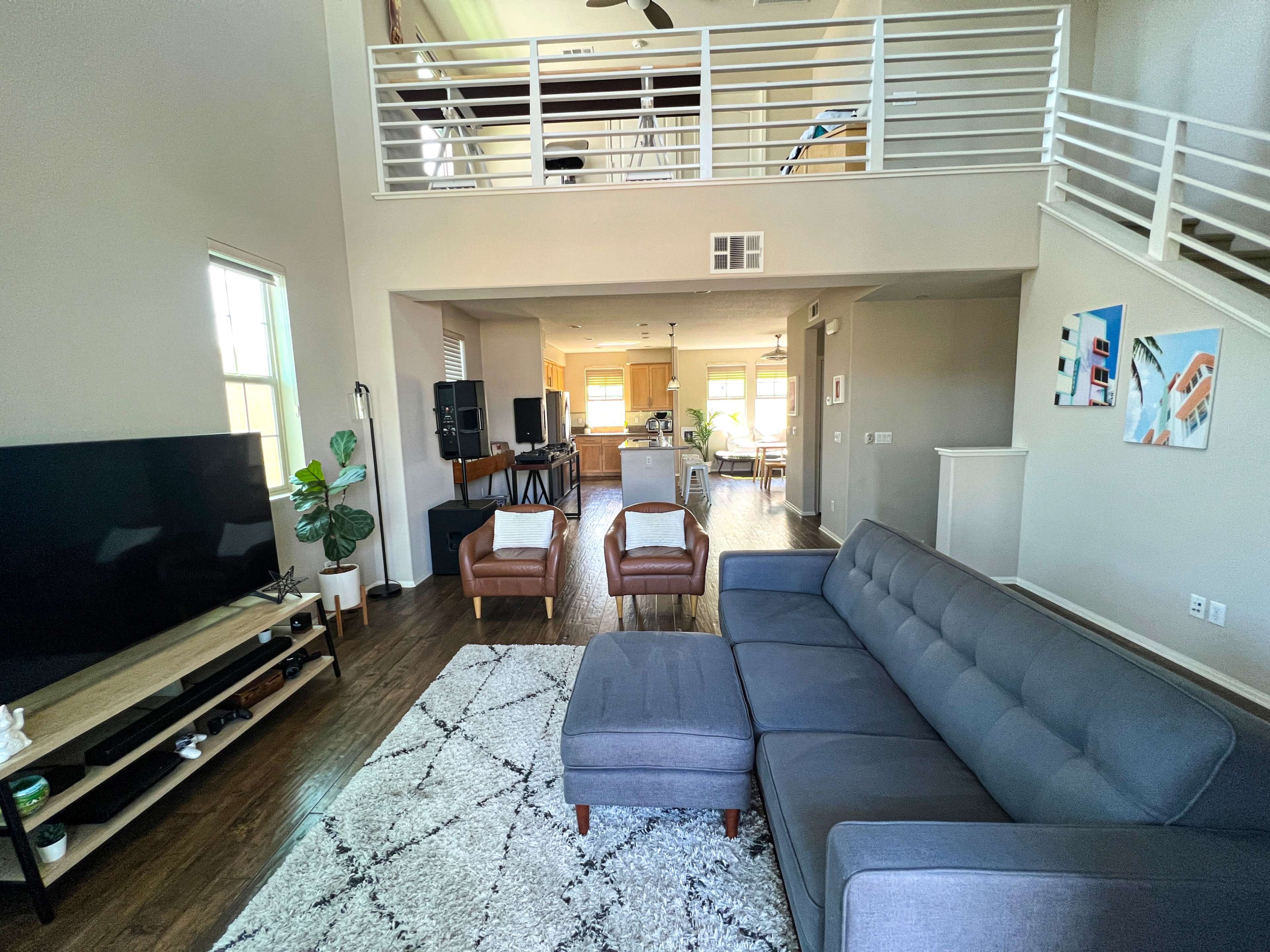 A modern living room with a gray sectional sofa, a television stand, and a view into an adjacent open kitchen and dining area.