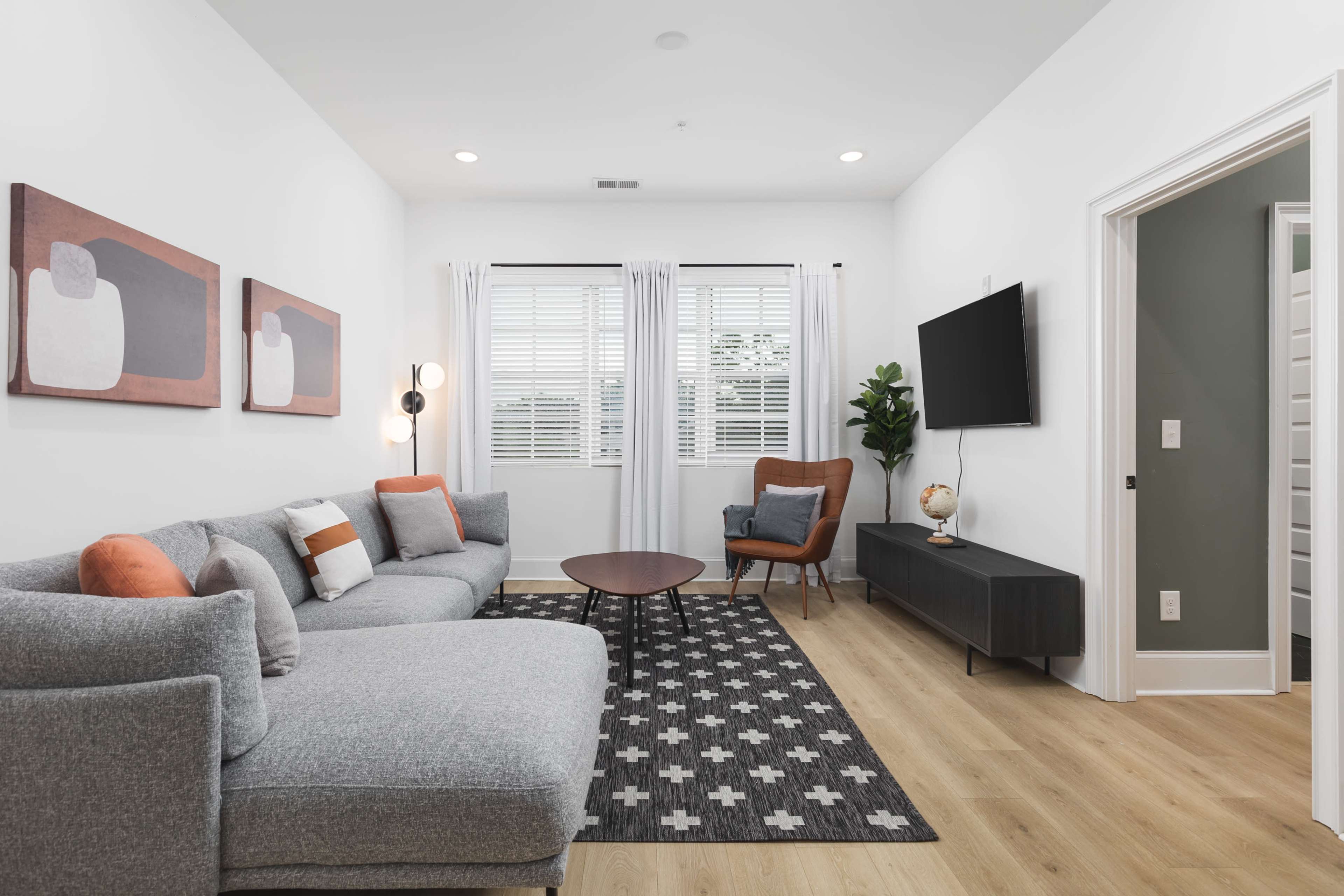 A modern living room features a gray sectional sofa, a round coffee table, and a large wall-mounted television, complemented by artwork and a potted plant.