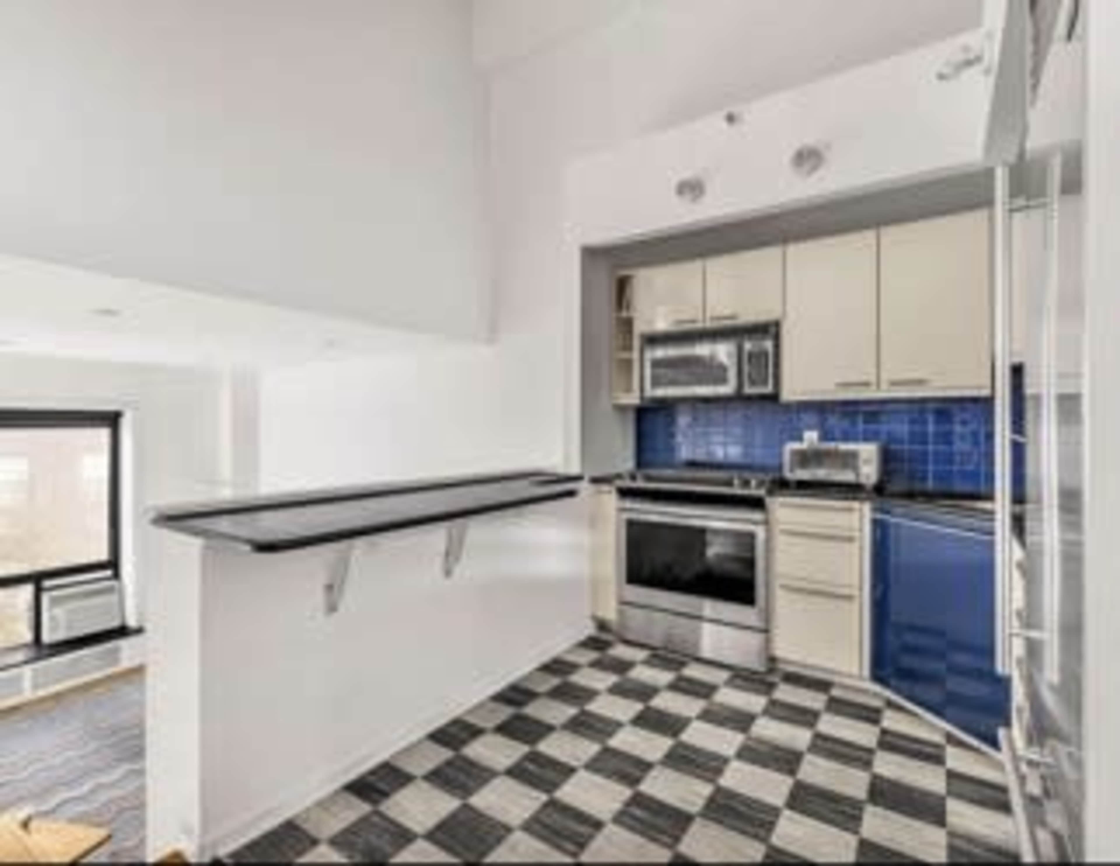 The image shows a modern kitchen with a black and white checkered floor, blue tiled backsplash, and stainless steel appliances.