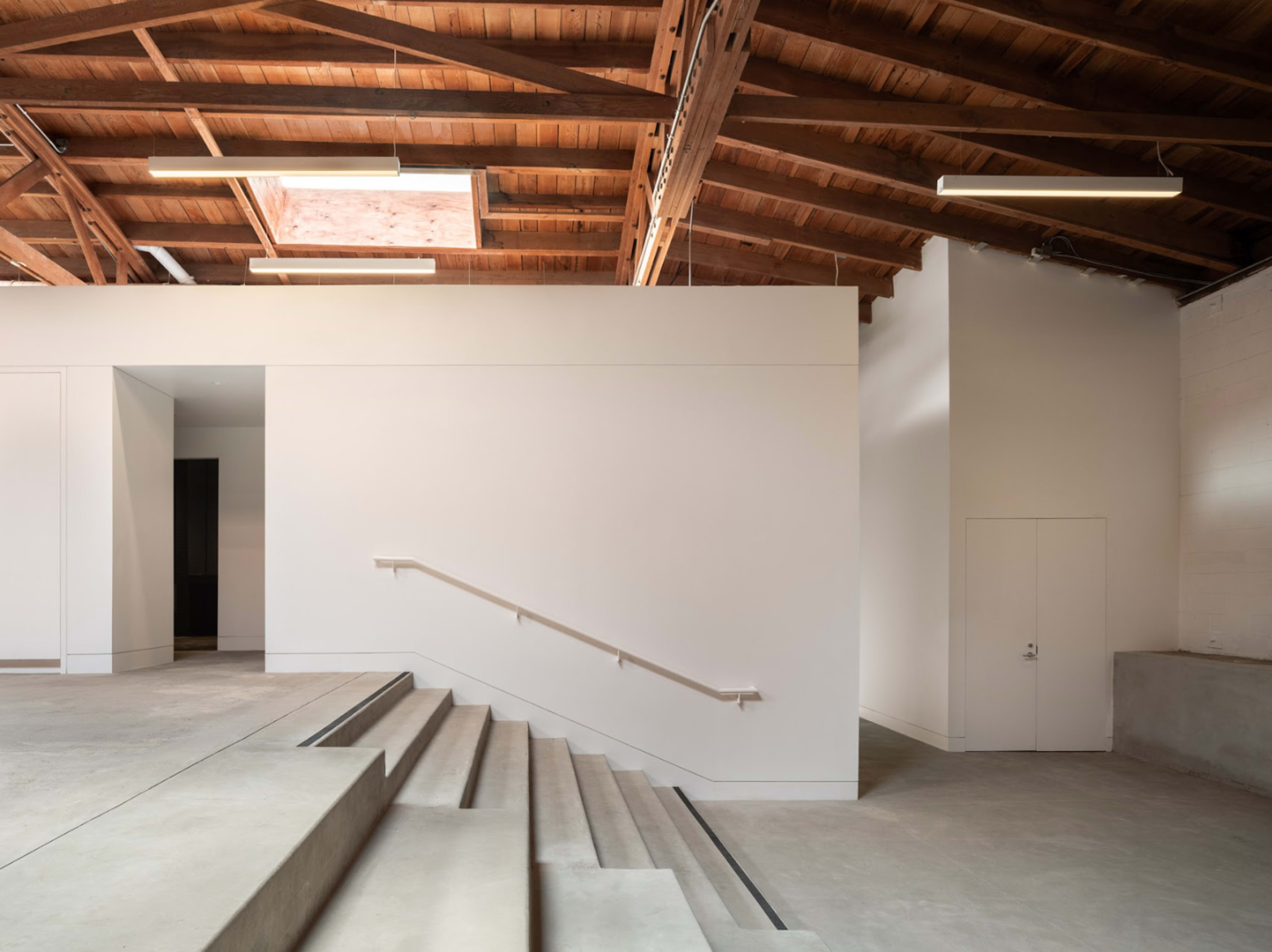 A modern interior space with a high wooden ceiling, a set of concrete steps leading to a doorway, and minimalistic white walls.