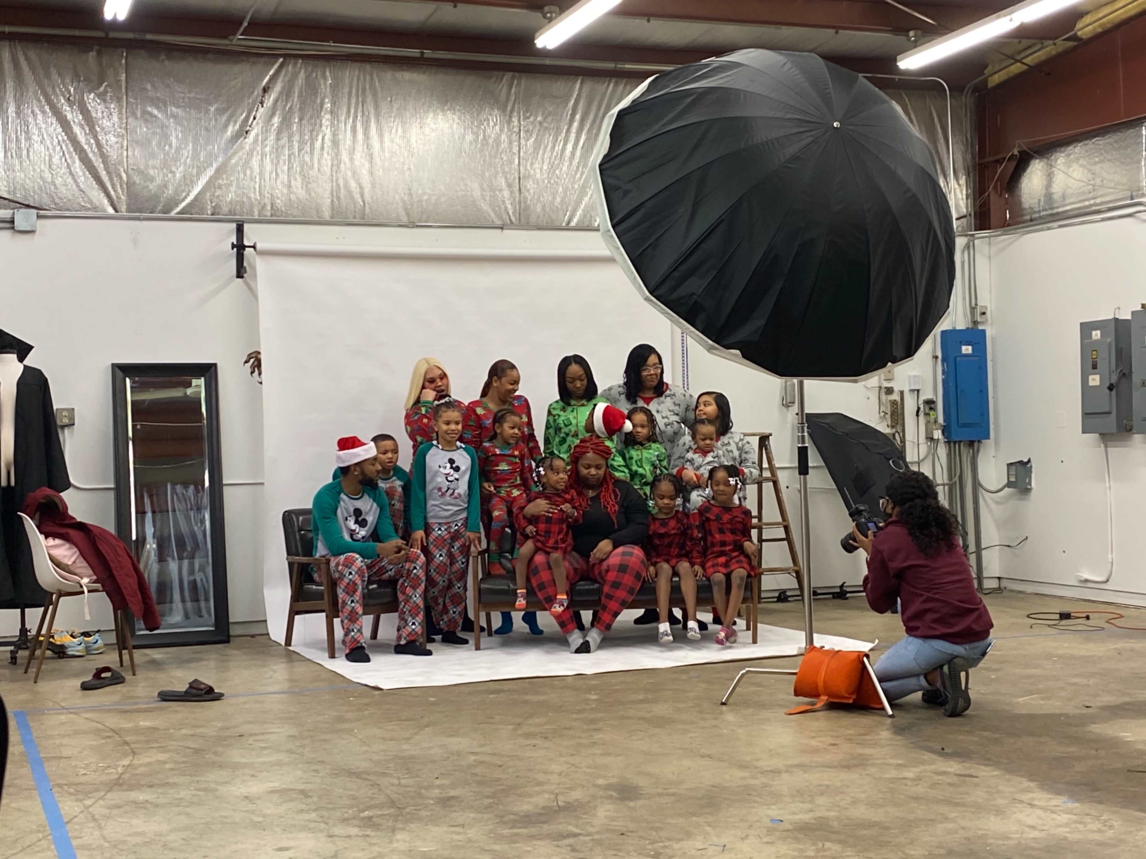 A group of people wearing matching holiday pajamas poses for a family photo in a studio setting with a large umbrella light.