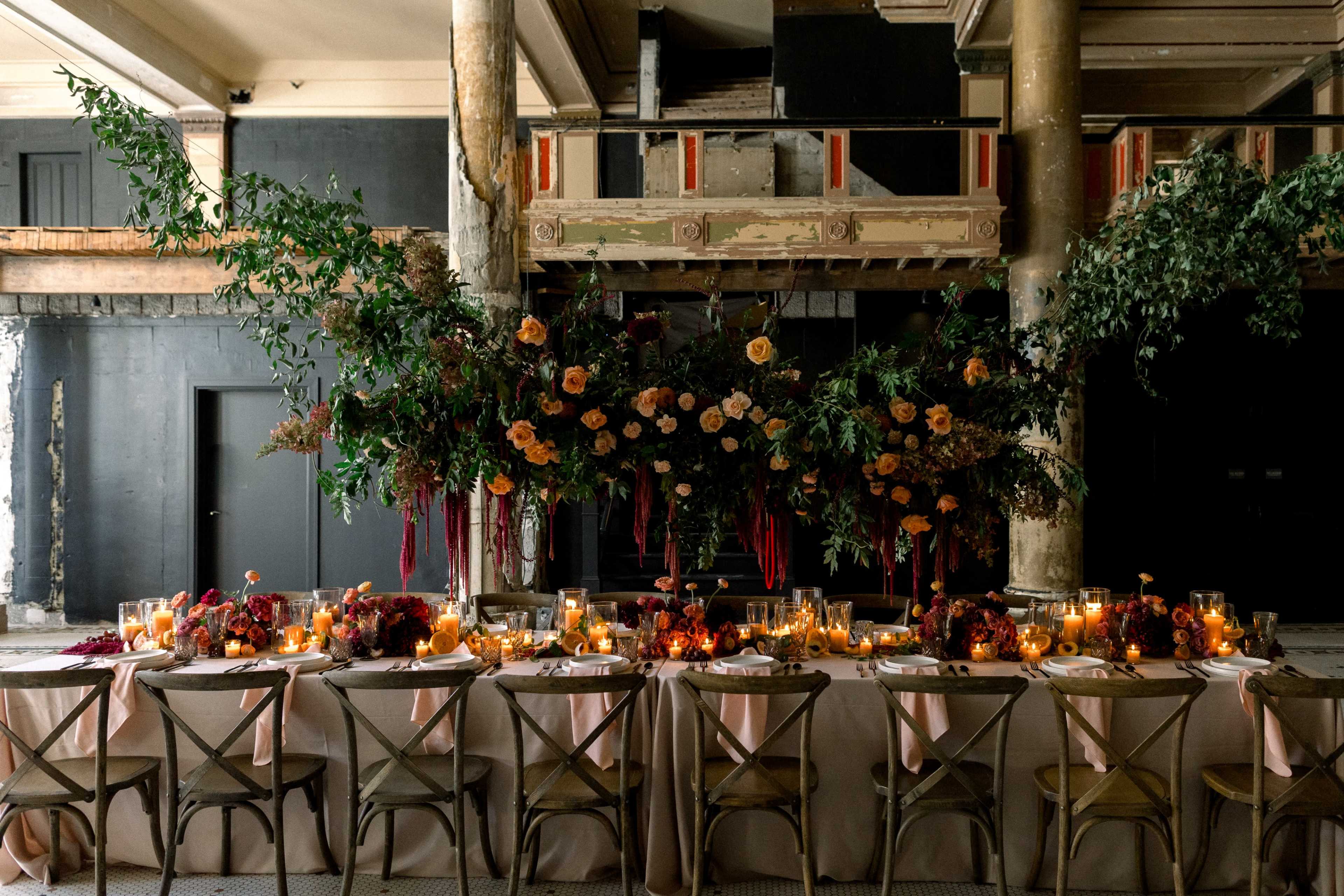 A long table is elegantly set with flowers, candles, and greenery in a spacious, partially renovated venue.