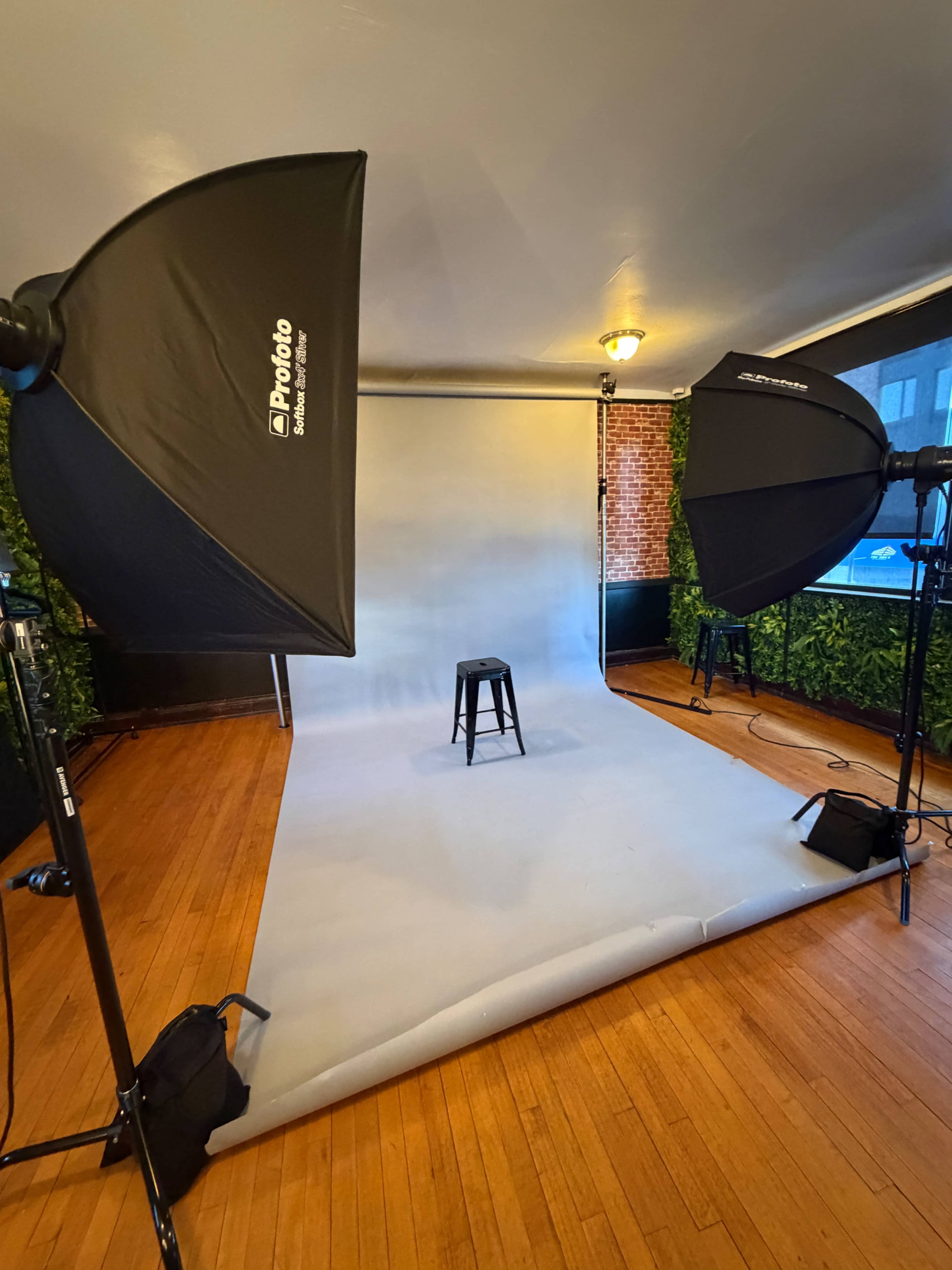 The image shows a photography studio setup with two softbox lights facing a stool positioned in front of a gray backdrop.