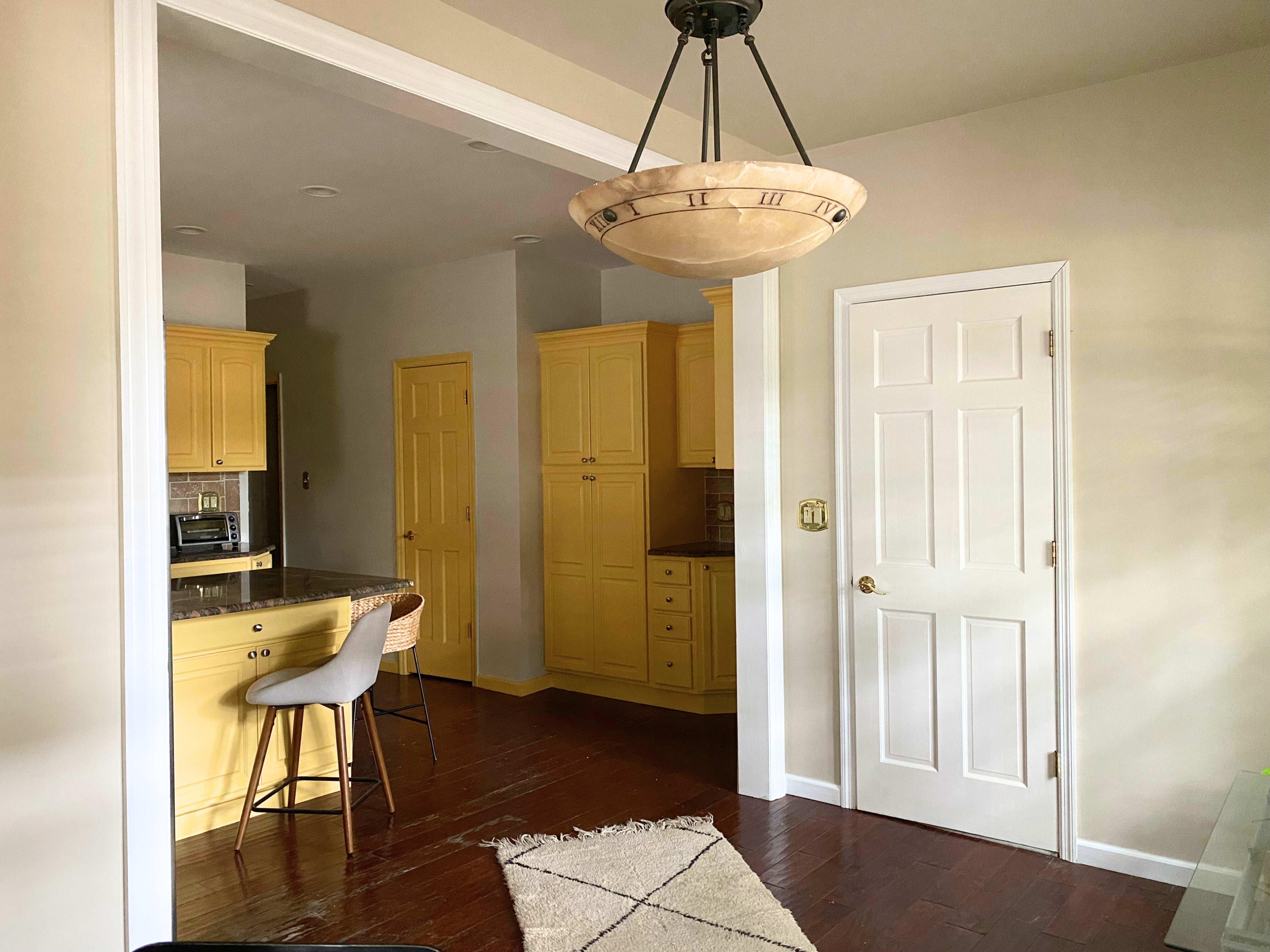 A kitchen area with yellow cabinets, a bar stool at a counter, and a door leading to another room.