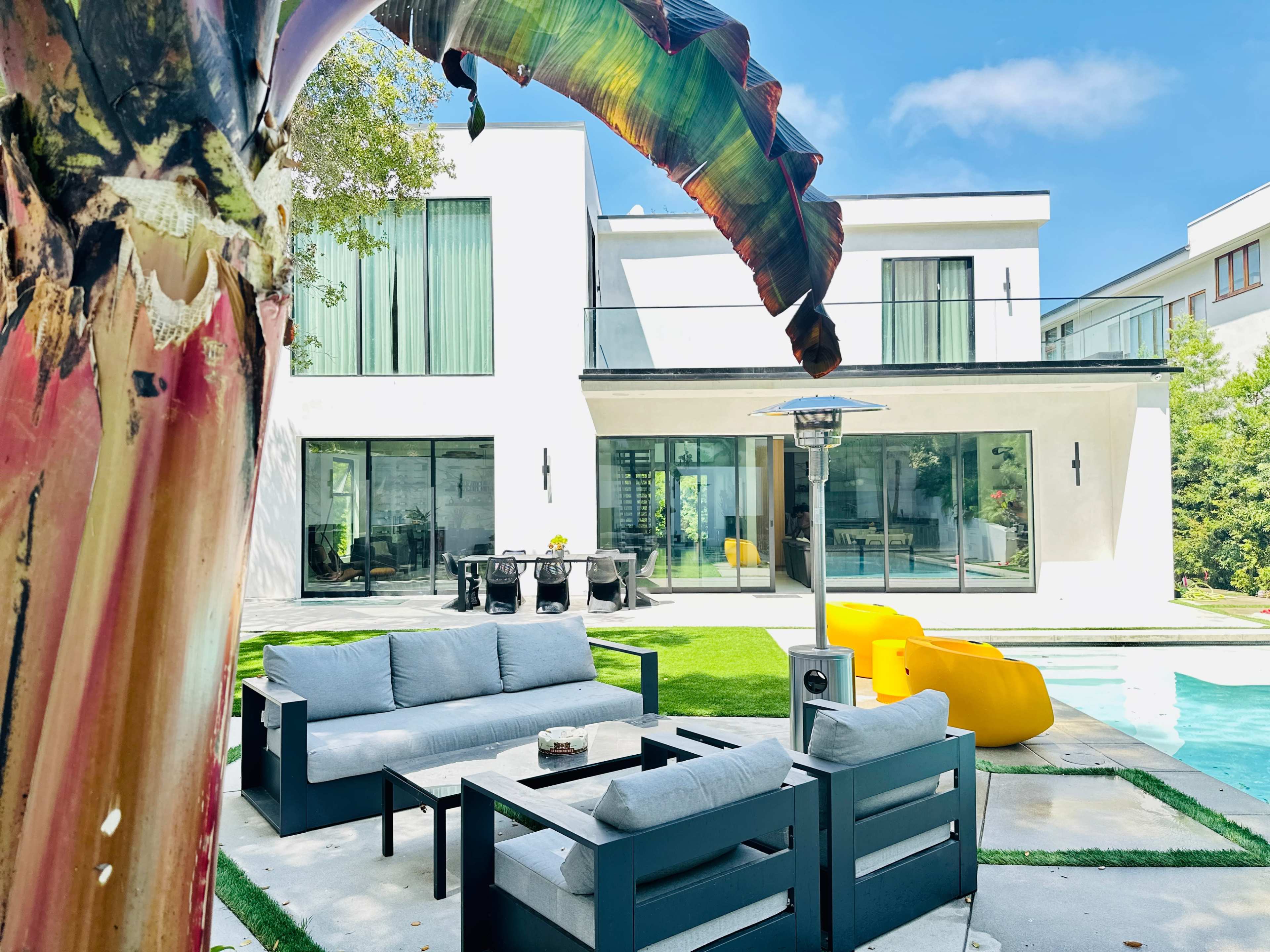 A modern backyard features a seating area with outdoor furniture, a swimming pool, and a two-story house in the background.