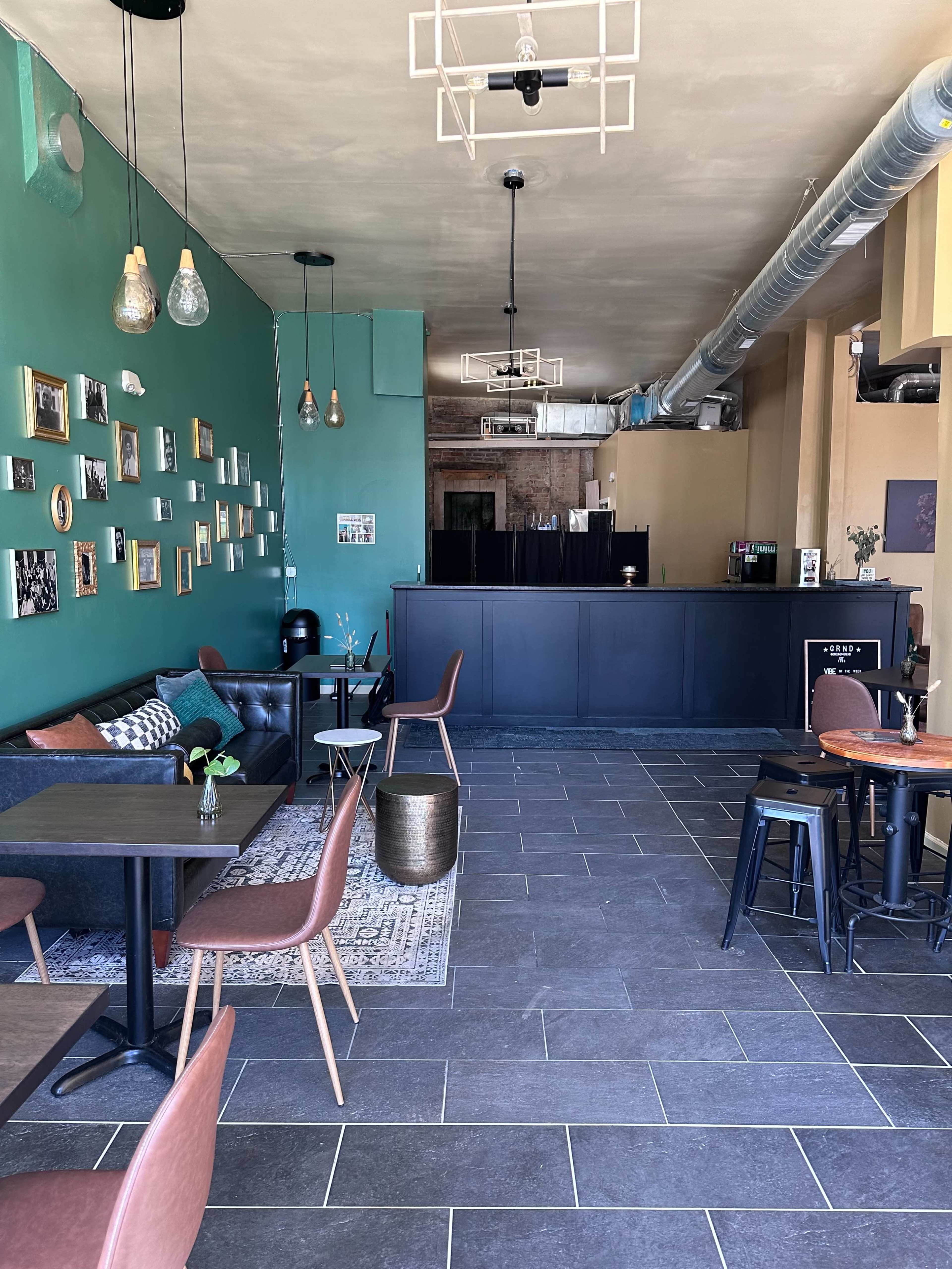 A cafe interior with green walls, a black counter, and a mix of seating options, including a leather sofa and metal chairs.