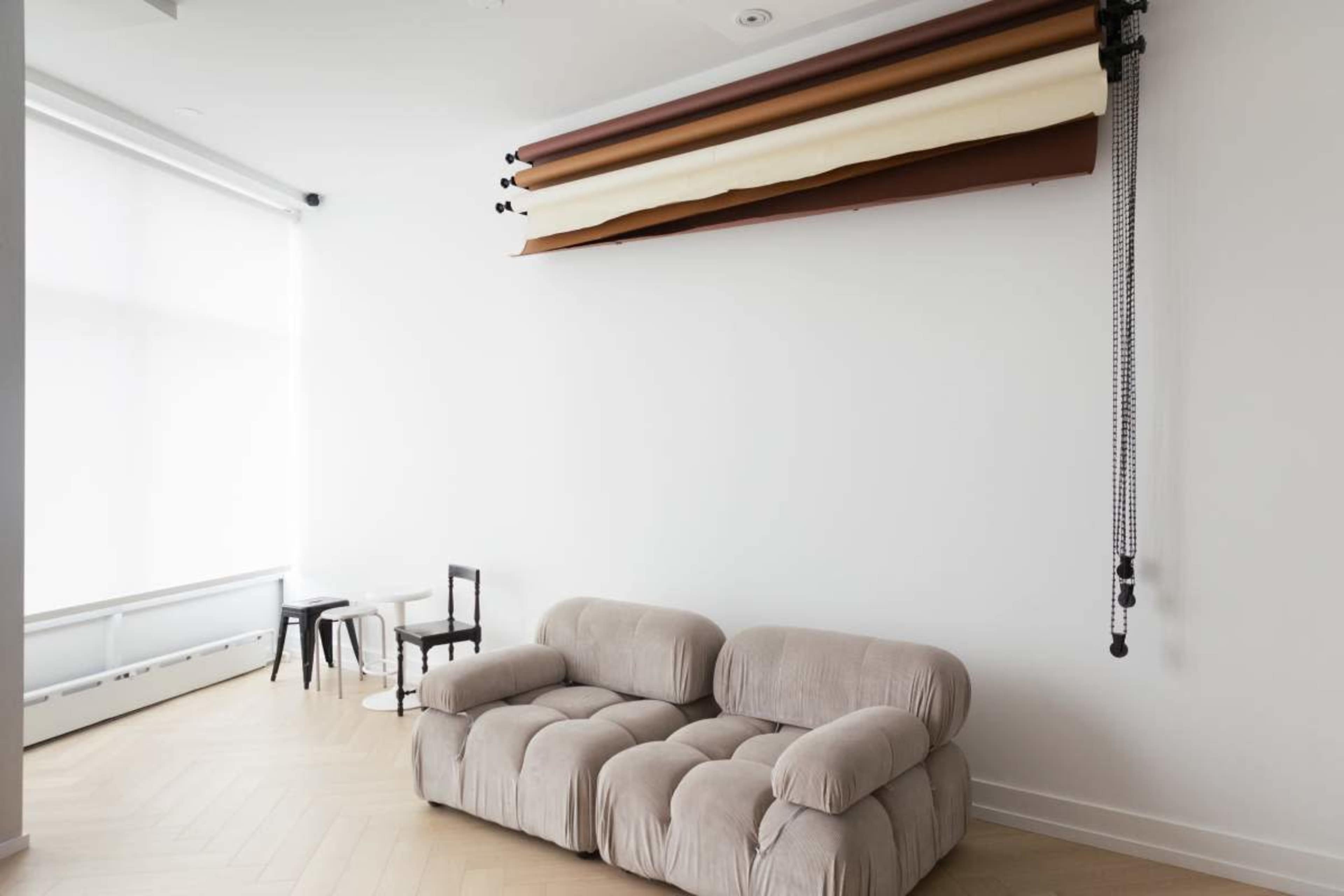 The image shows a modern living space featuring a light-colored couch, a couple of small tables, and a backdrop system mounted on the wall.