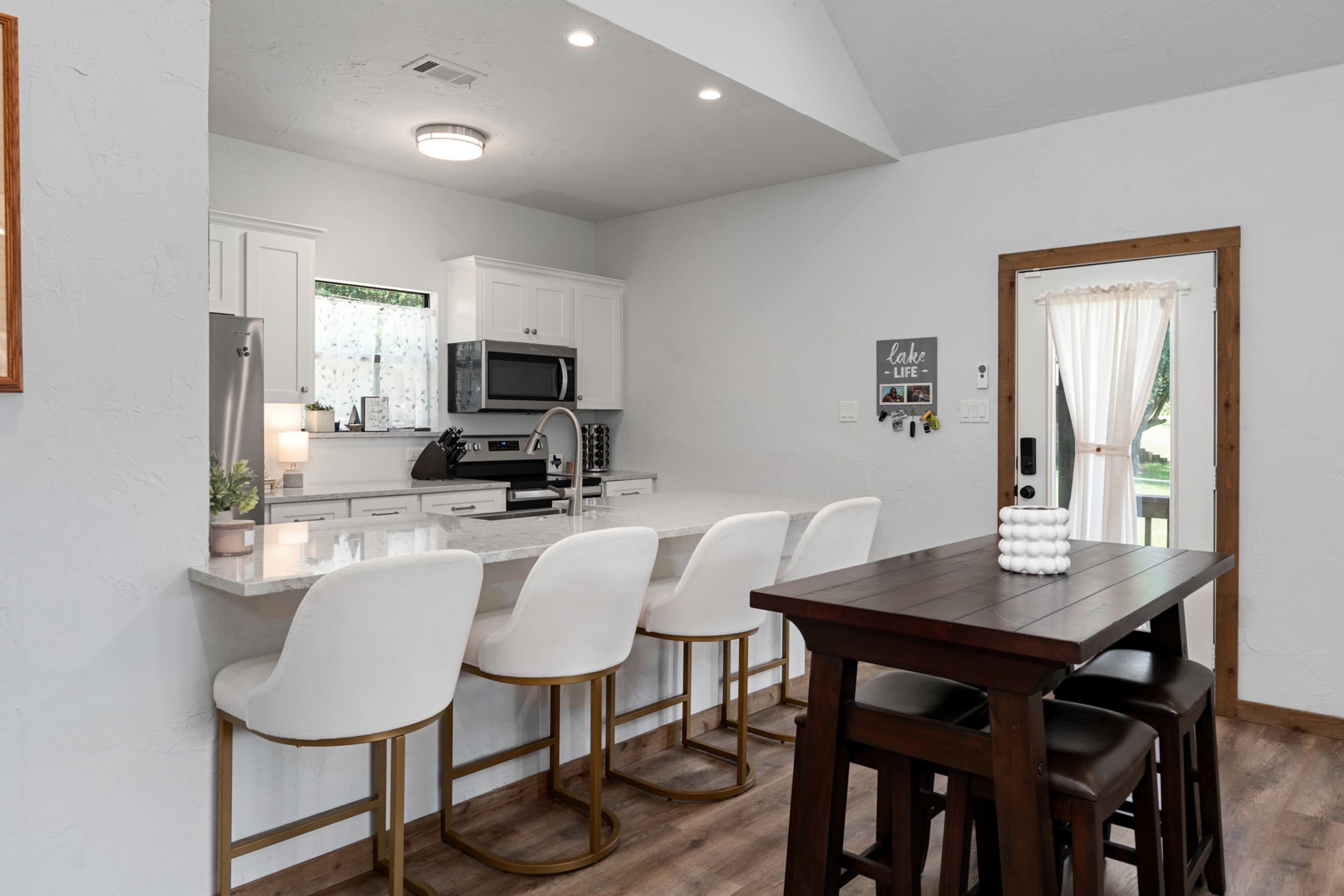 A modern kitchen features white cabinetry, stainless steel appliances, and a dining area with a dark wood table and bar seating.