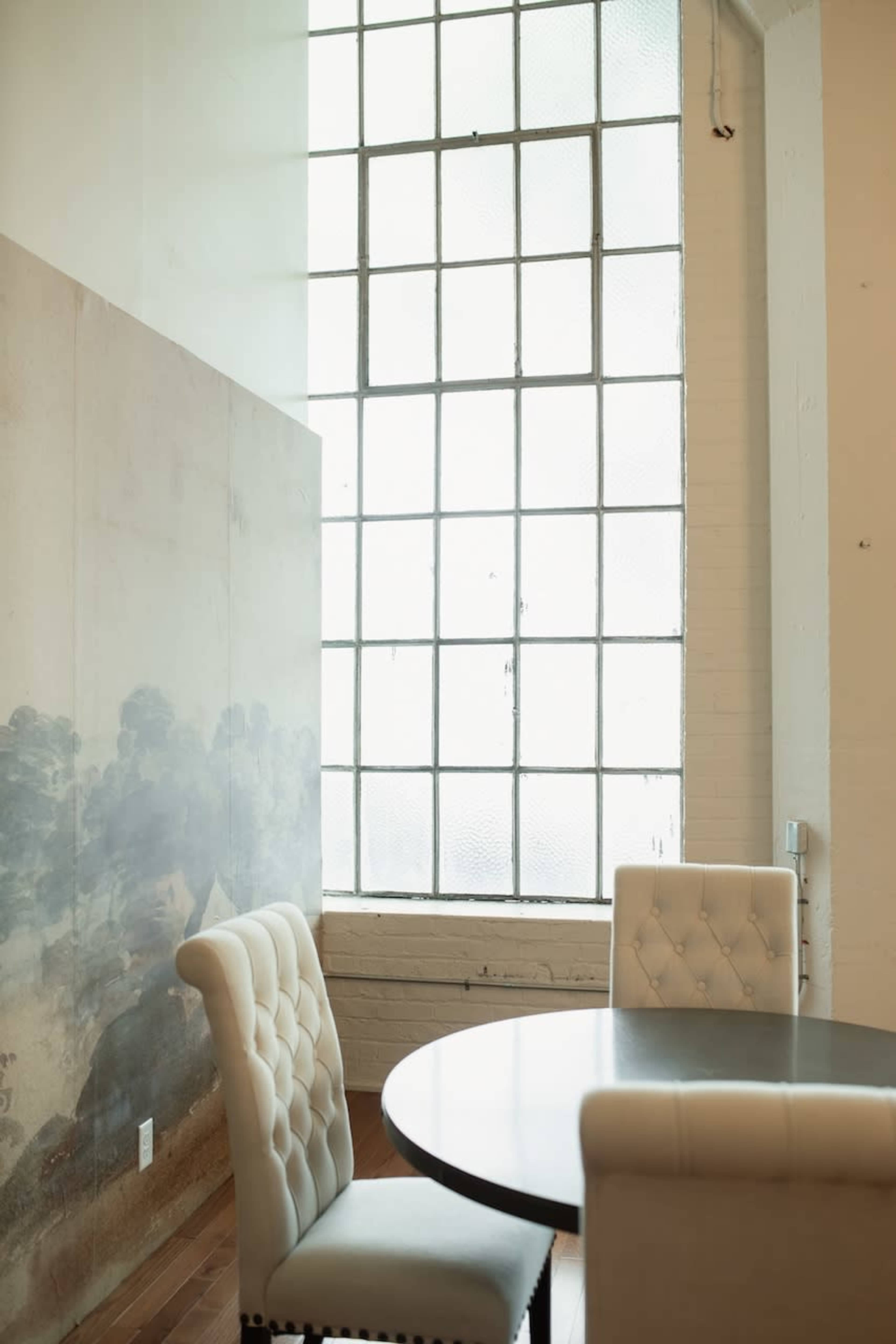 A bright room features a round table with two upholstered chairs beside a large window with a grid design.