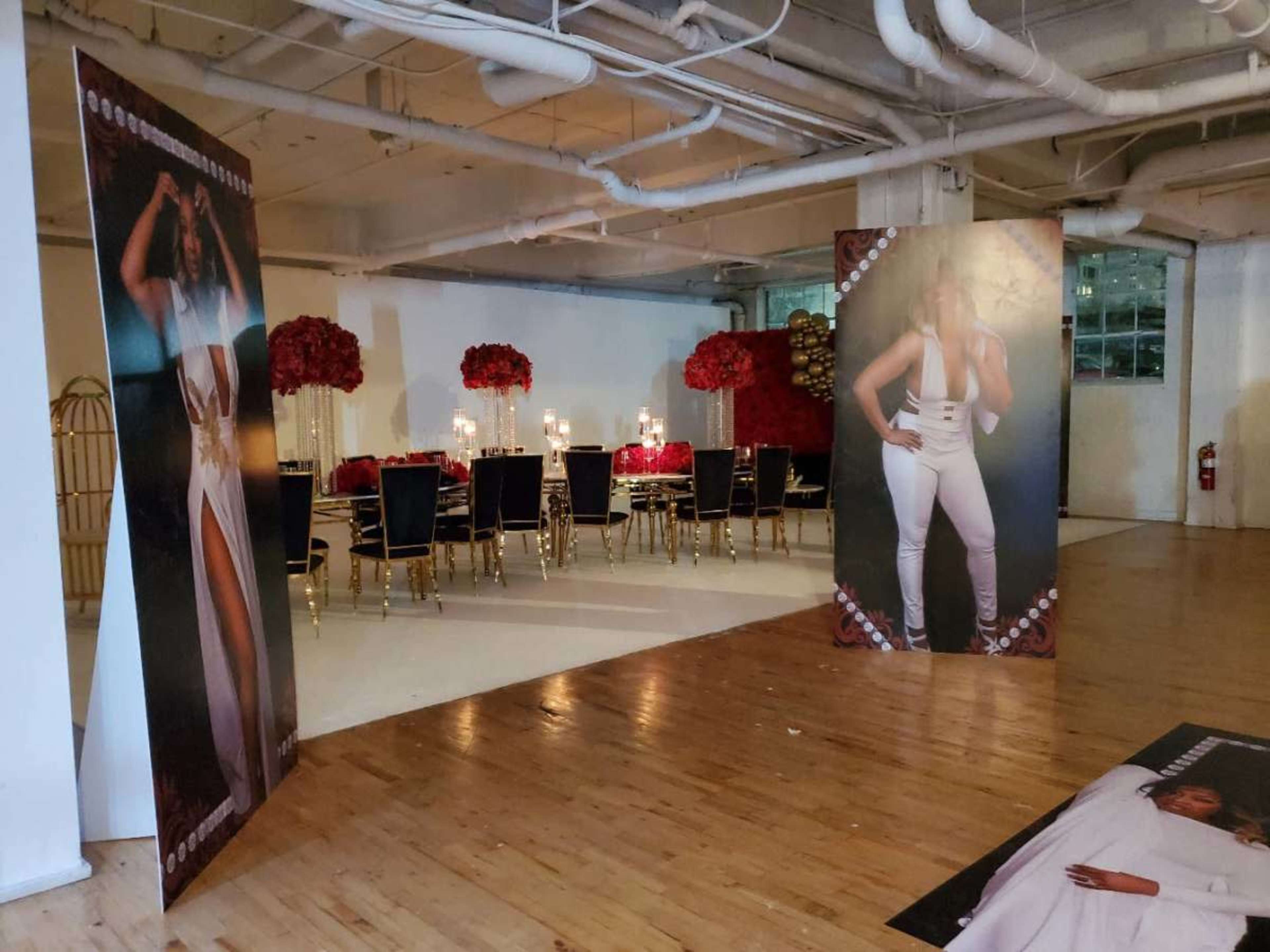 A spacious event room with large banners featuring a figure on either side, a dining table set for guests, and floral arrangements in the center.