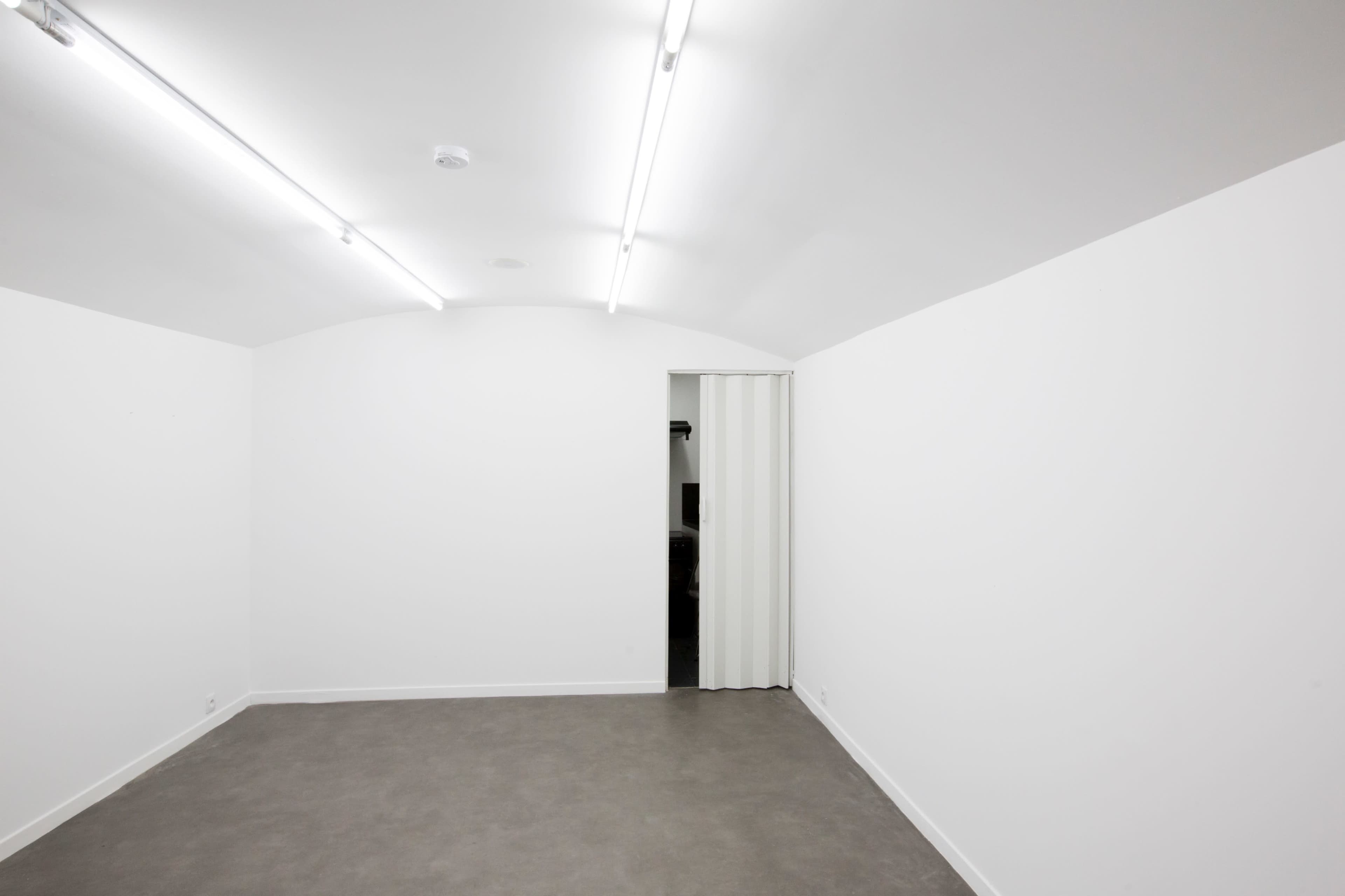 The image shows a minimalist, dimly lit room with an arched ceiling and a door partially open on one wall.