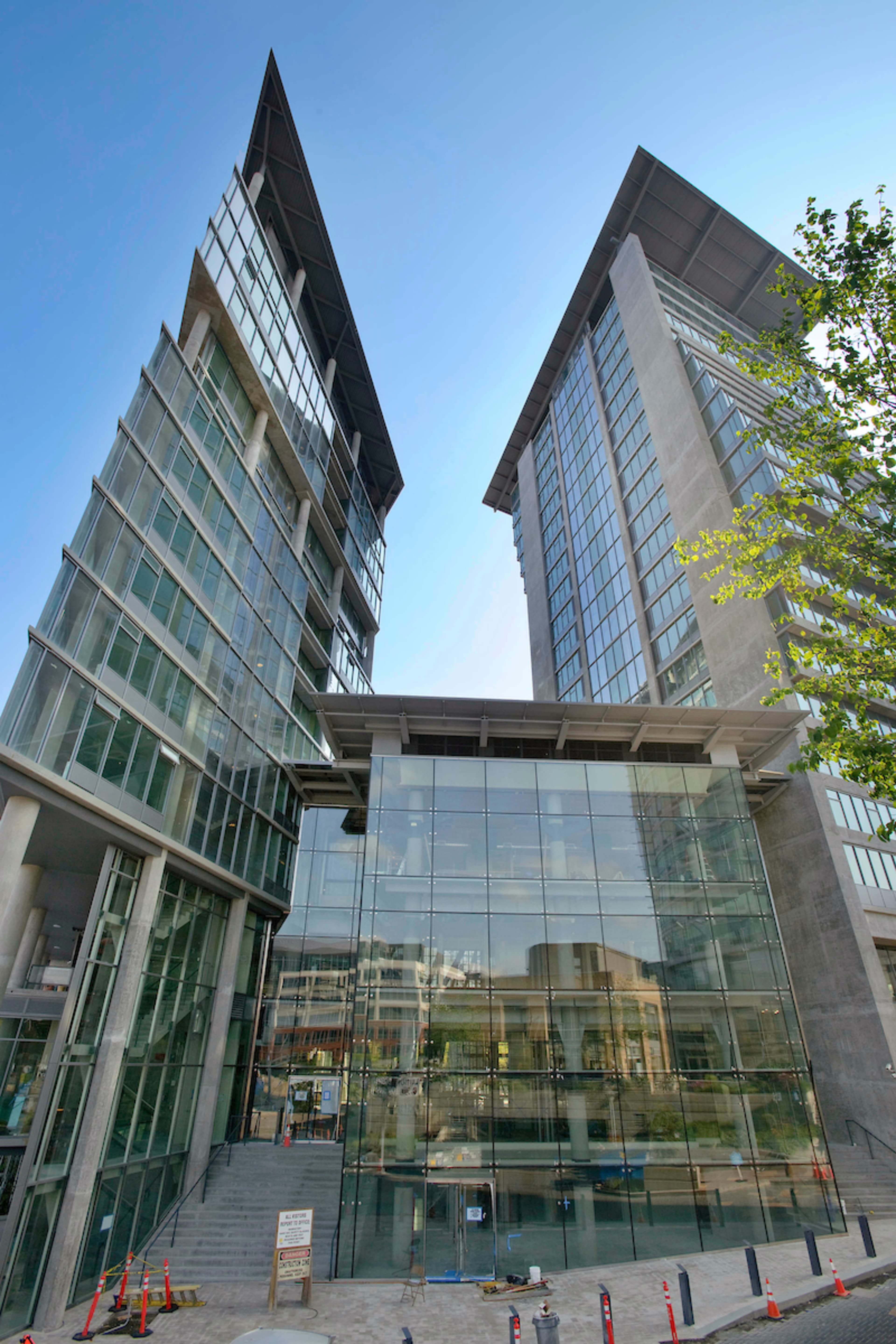 A pair of modern glass and concrete office buildings with angular designs and a clear blue sky above.
