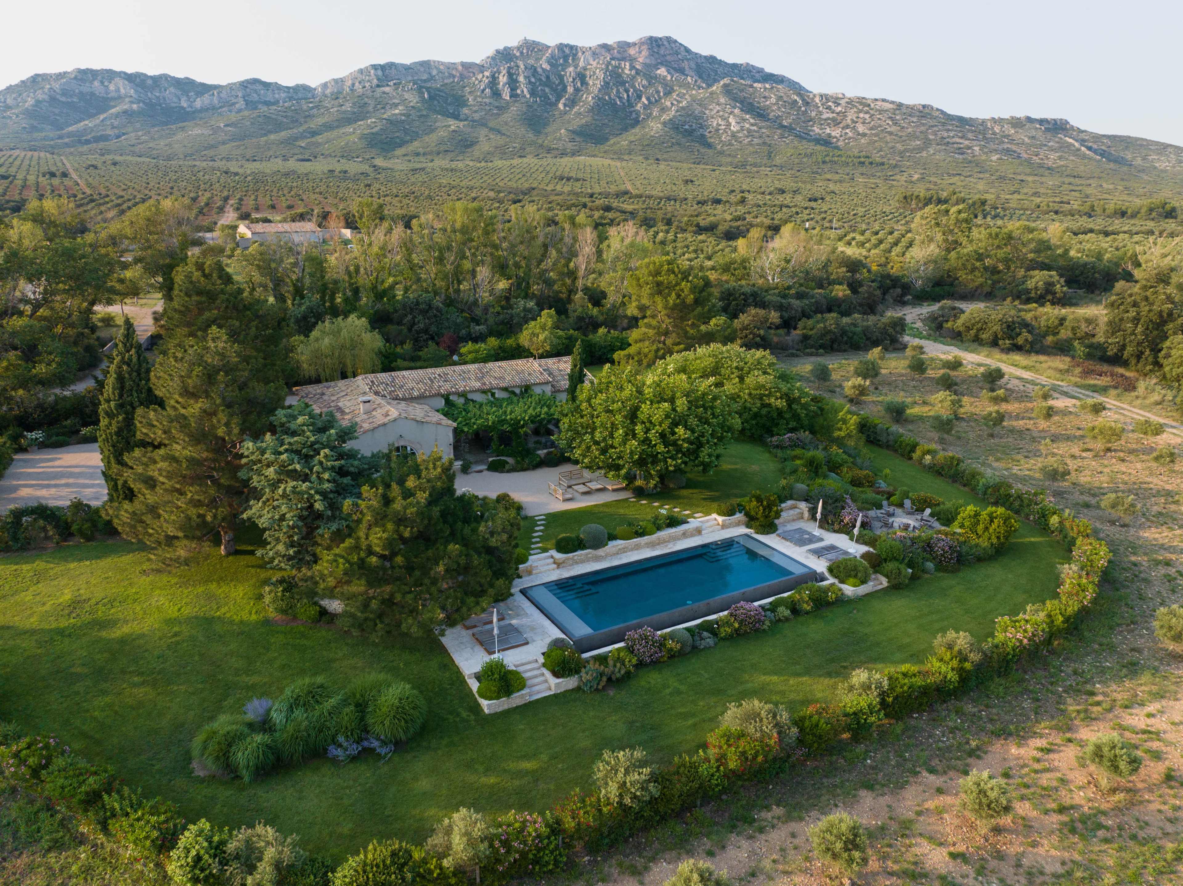 A tranquil villa surrounded by lush greenery and a rectangular swimming pool, set against a backdrop of mountains and orchards.