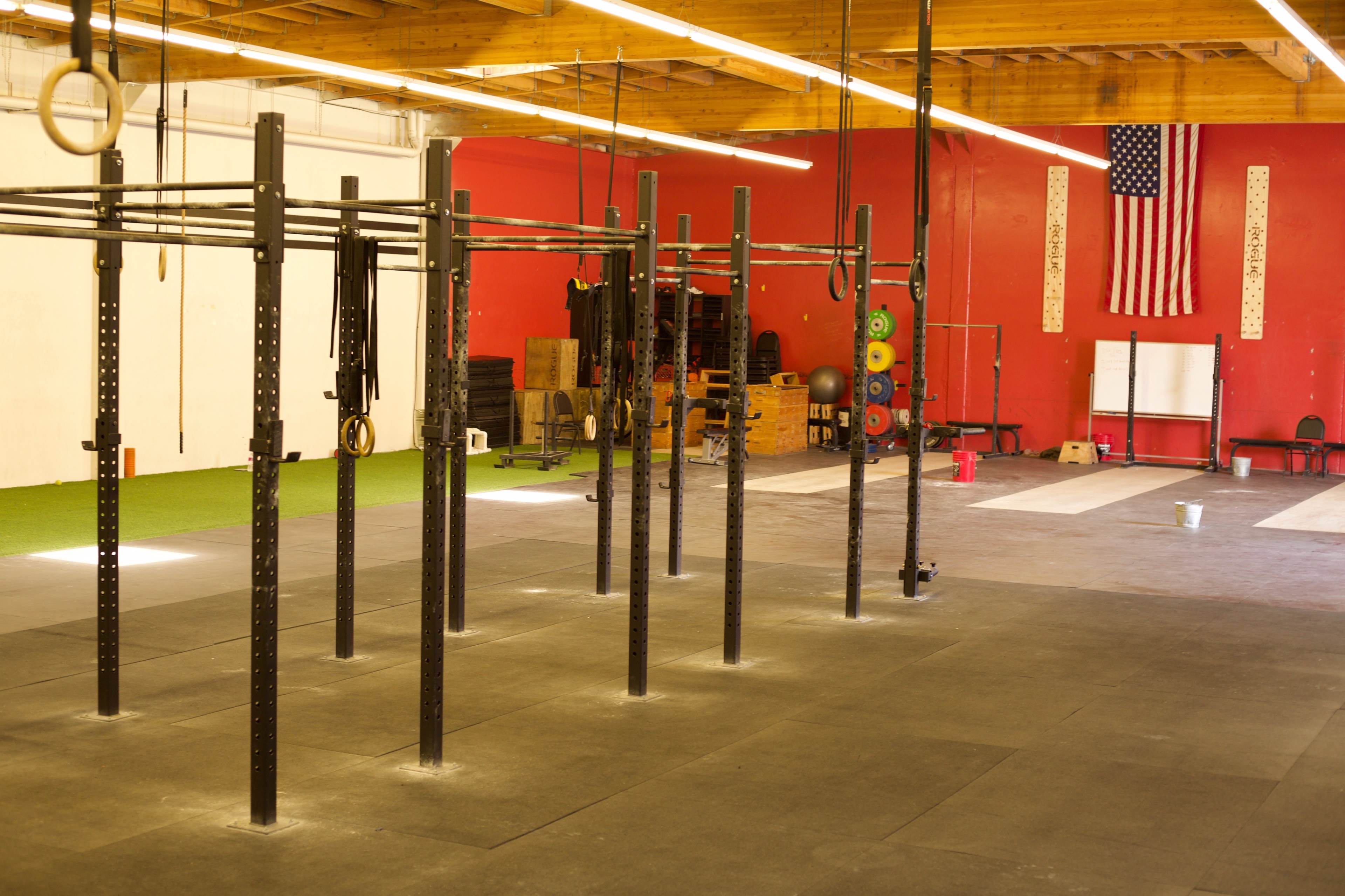 The image shows a spacious gym with a red wall, various exercise equipment, and an American flag hanging in the background.