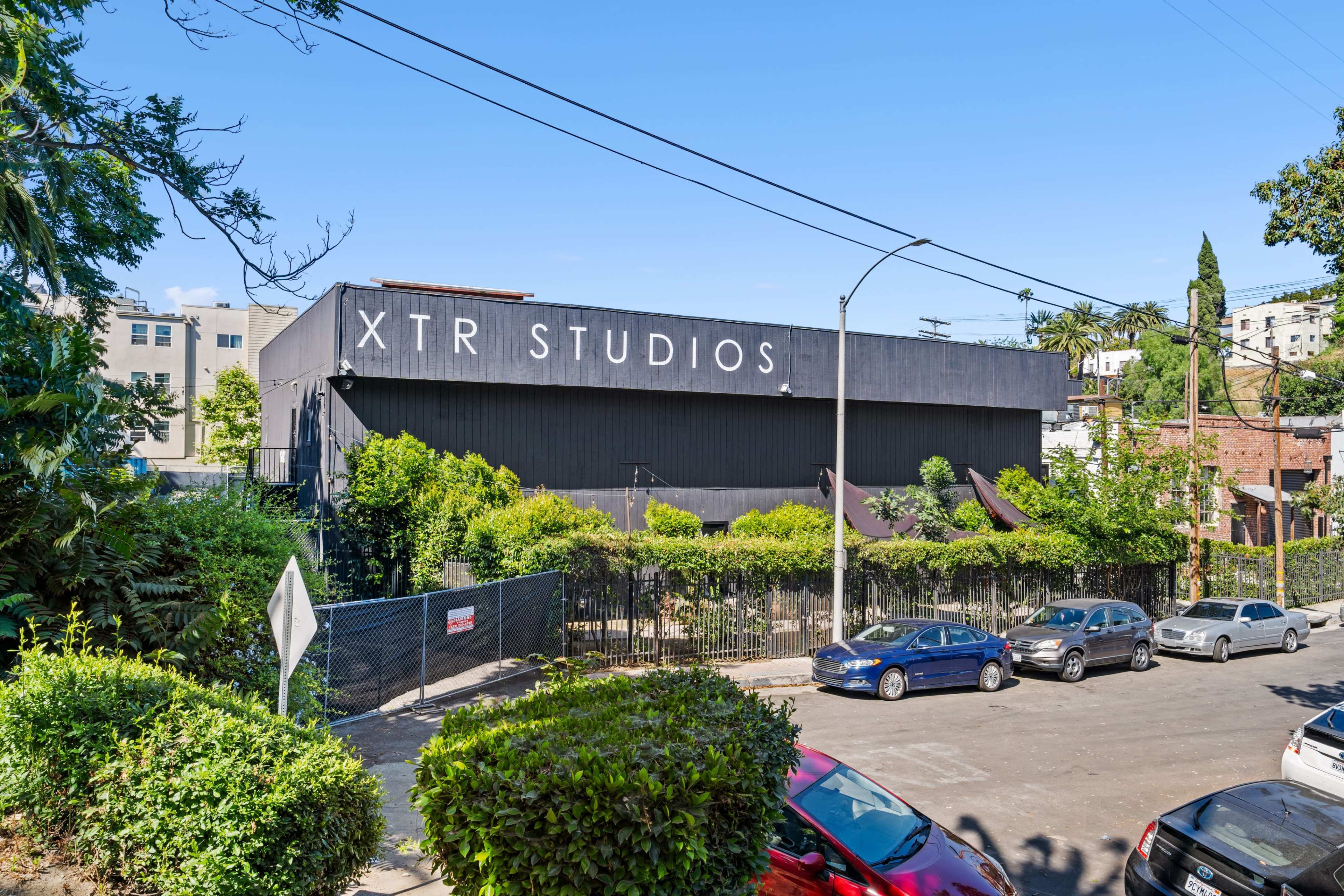 Xtr Studios, a large black building surrounded by greenery and parked cars on a street.