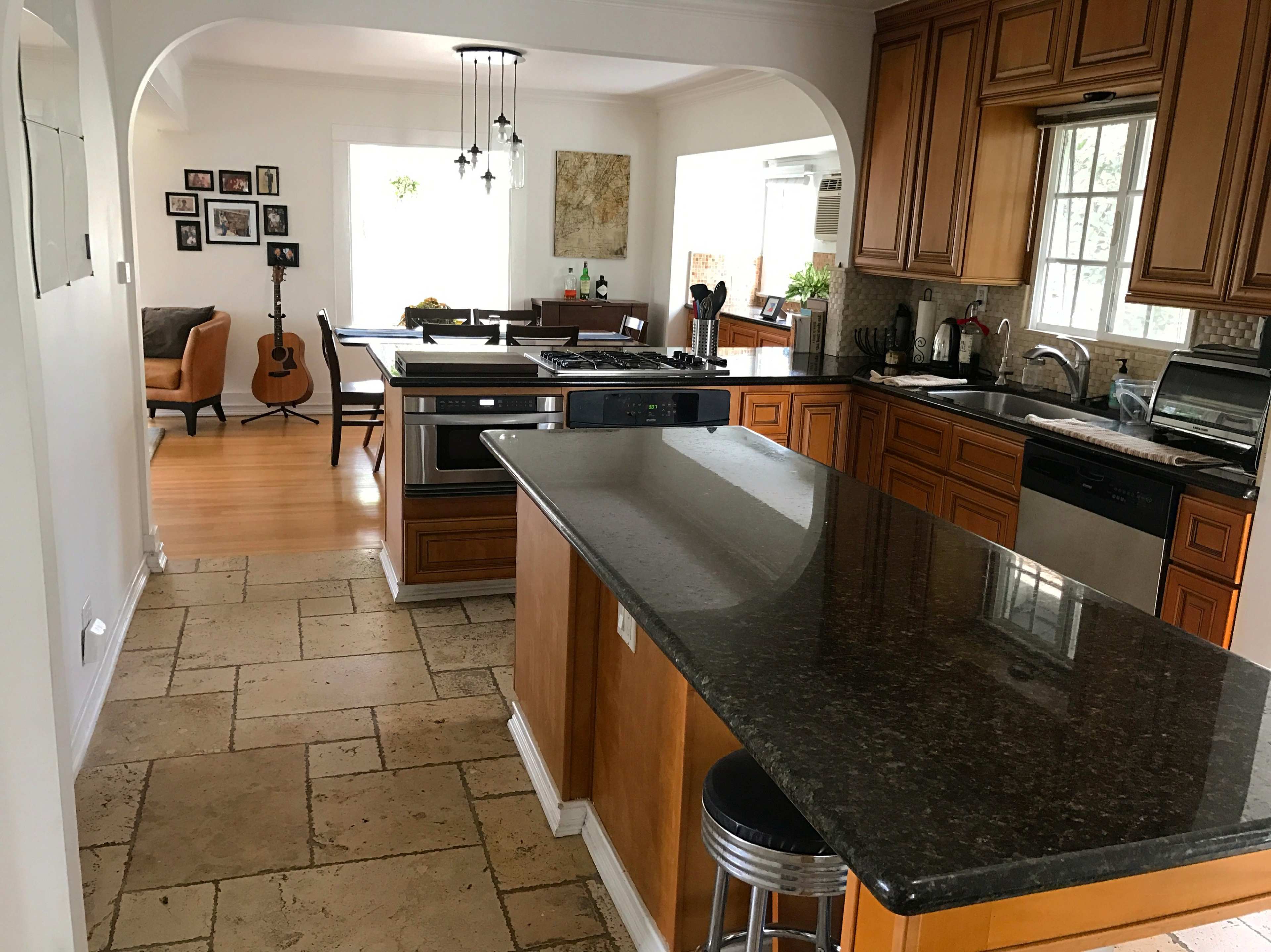 The image shows a spacious kitchen with dark countertops, wooden cabinetry, and an open layout leading to a dining area.