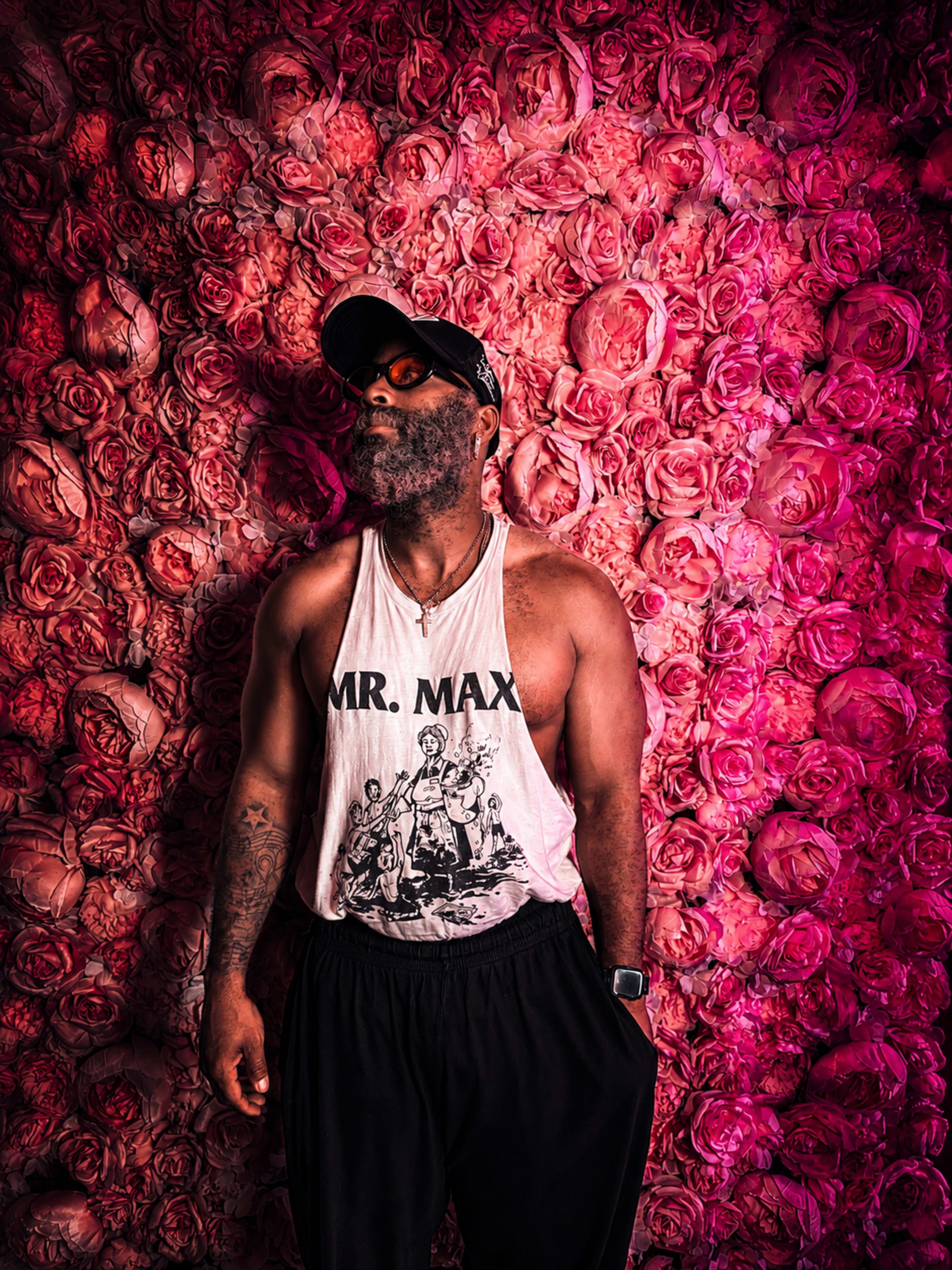 A man wearing a sleeveless shirt stands against a vibrant pink floral wall.