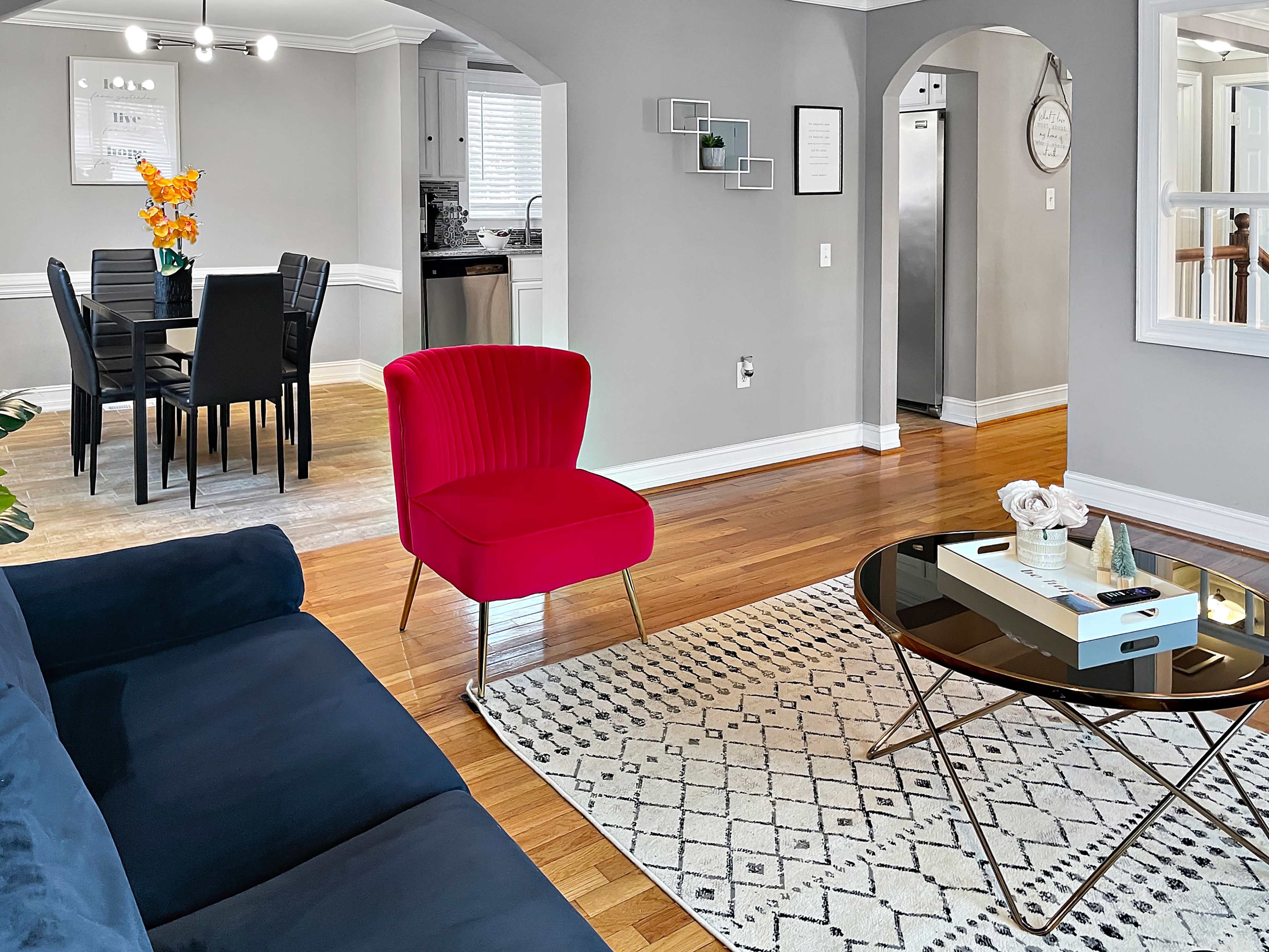 A living room with a navy blue sofa, a red chair, a glass coffee table, and a dining area in the background.