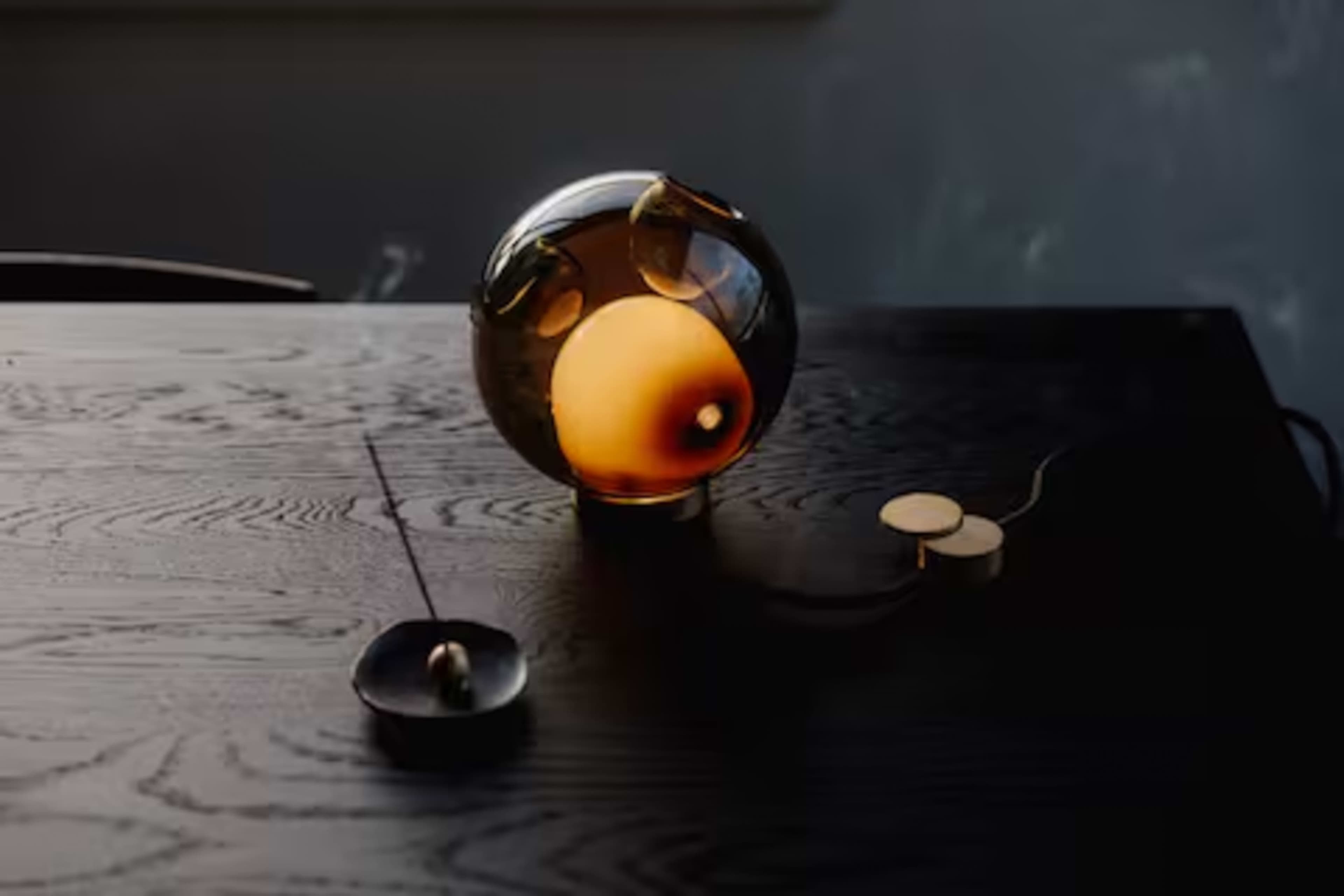 A glass orb lamp emits warm light on a wooden table next to a small dish and a round switch.