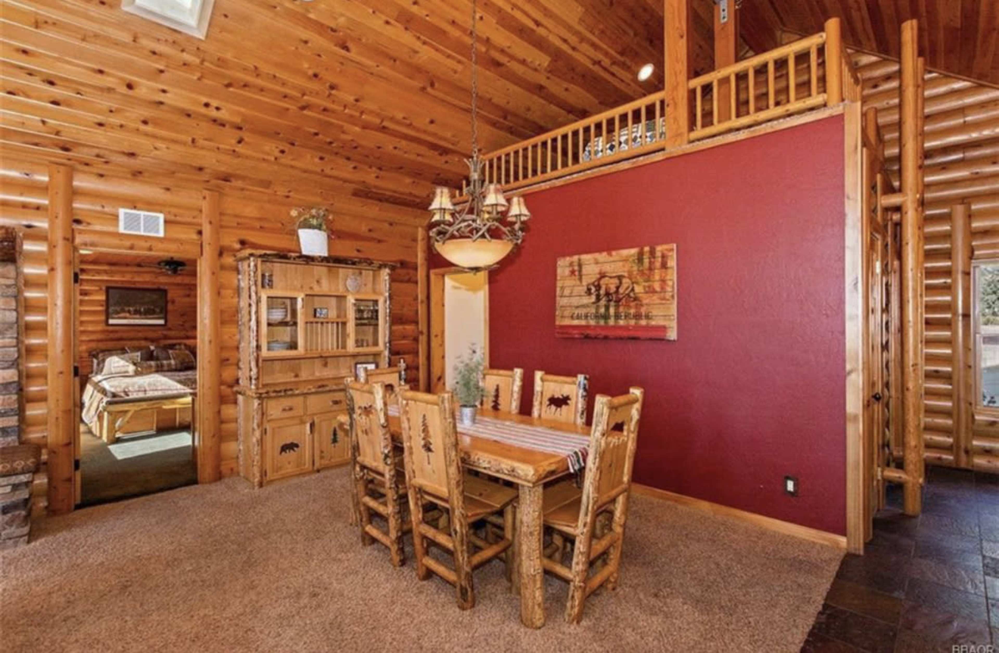 A wooden dining area with a rustic table and chairs, adjacent to a log cabin-style living room.