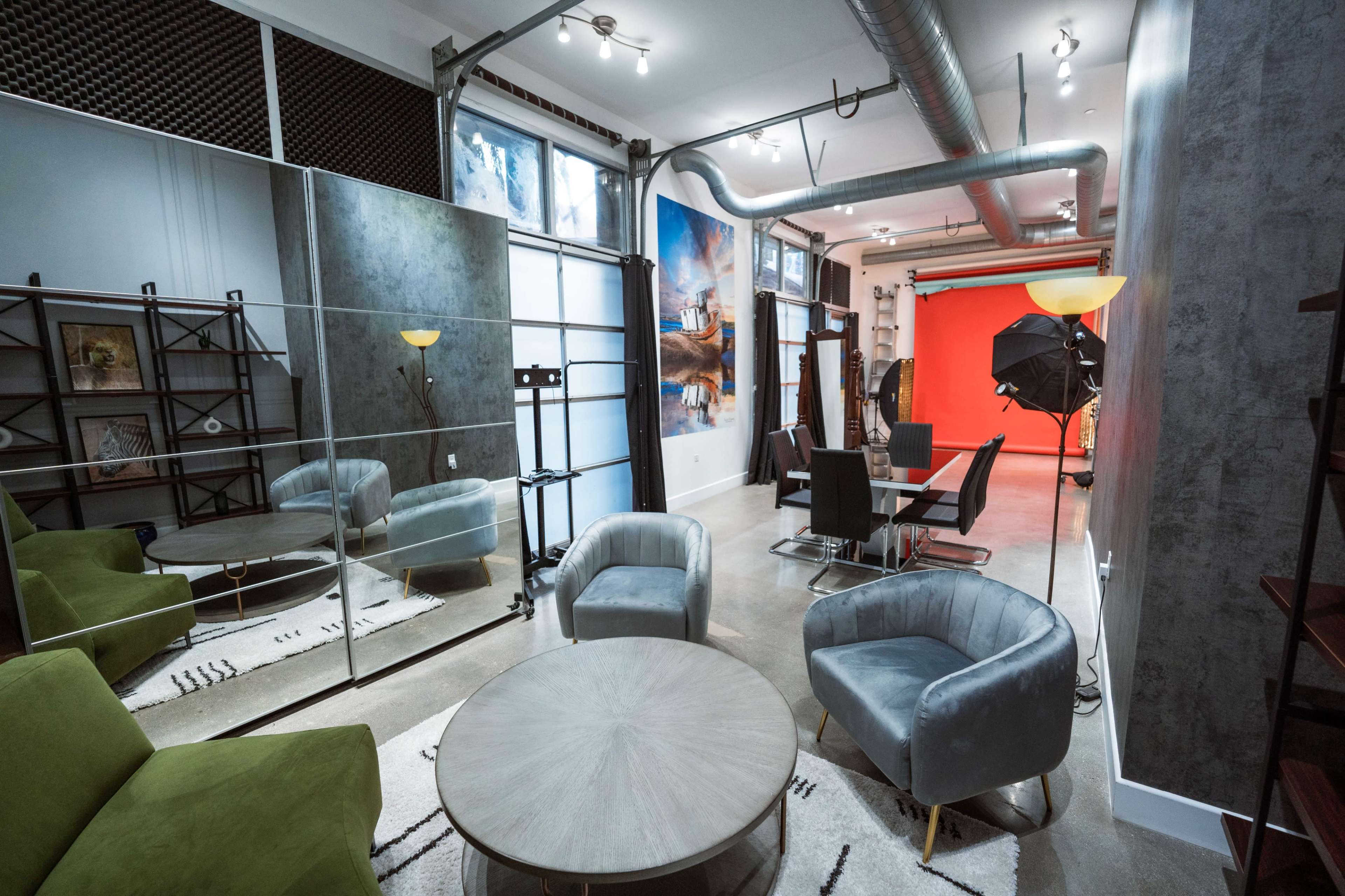 The image shows a modern studio space with green and gray chairs, a round coffee table, a mirrored wall, and various equipment for photography.