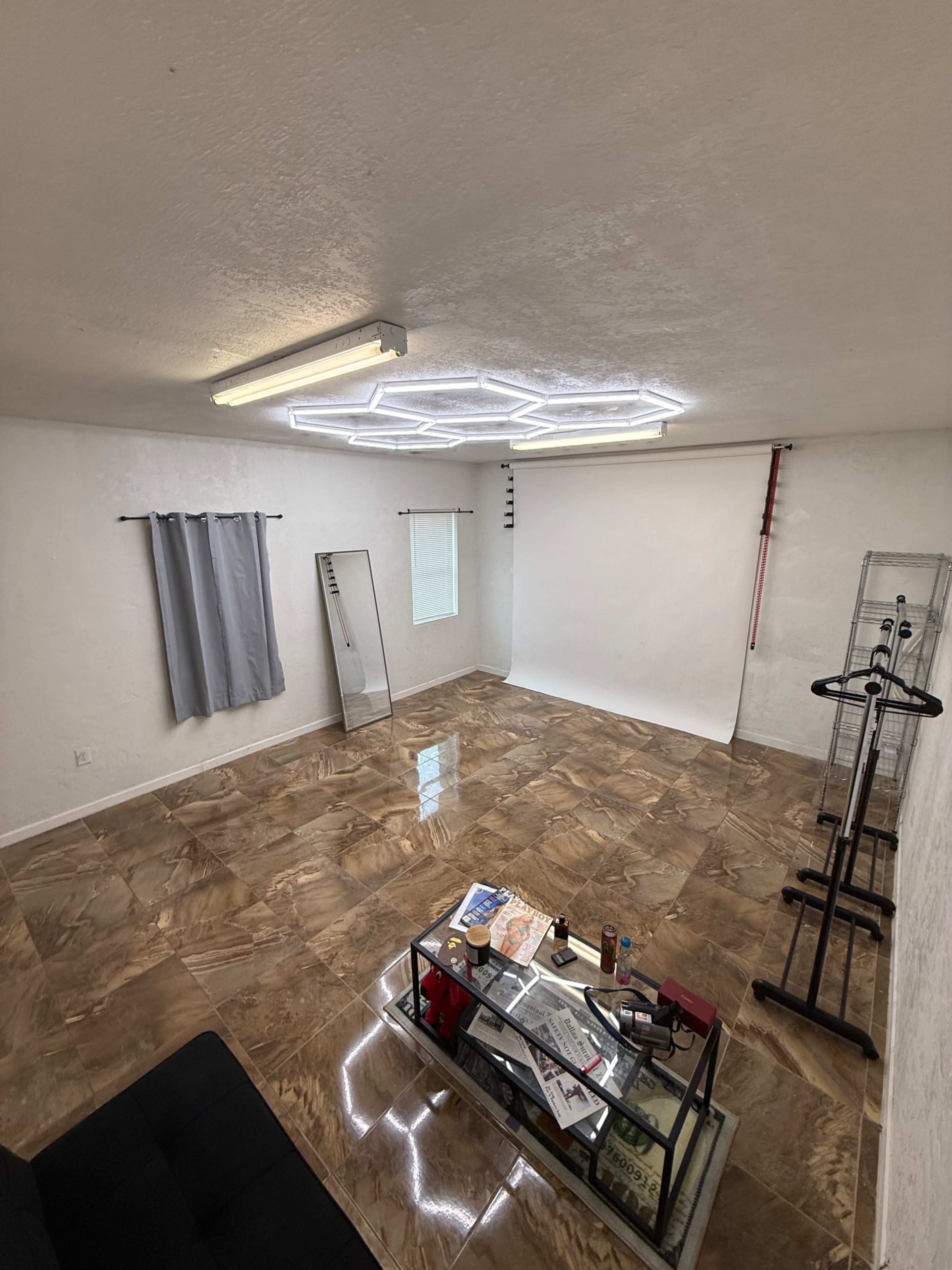 The room features a polished marble floor, a neutral-colored wall, and modern lighting, with a glass coffee table at the center and a backdrop setup against one wall.